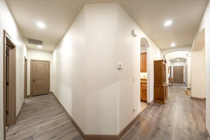 Hall featuring light wood finished floors, arched walkways, and recessed lighting
