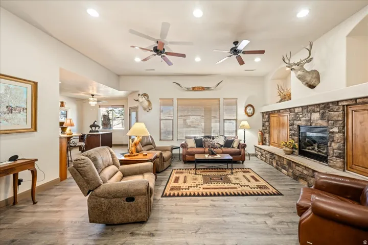 Living area featuring wood finished floors, a stone fireplace, ceiling fan, and recessed lighting