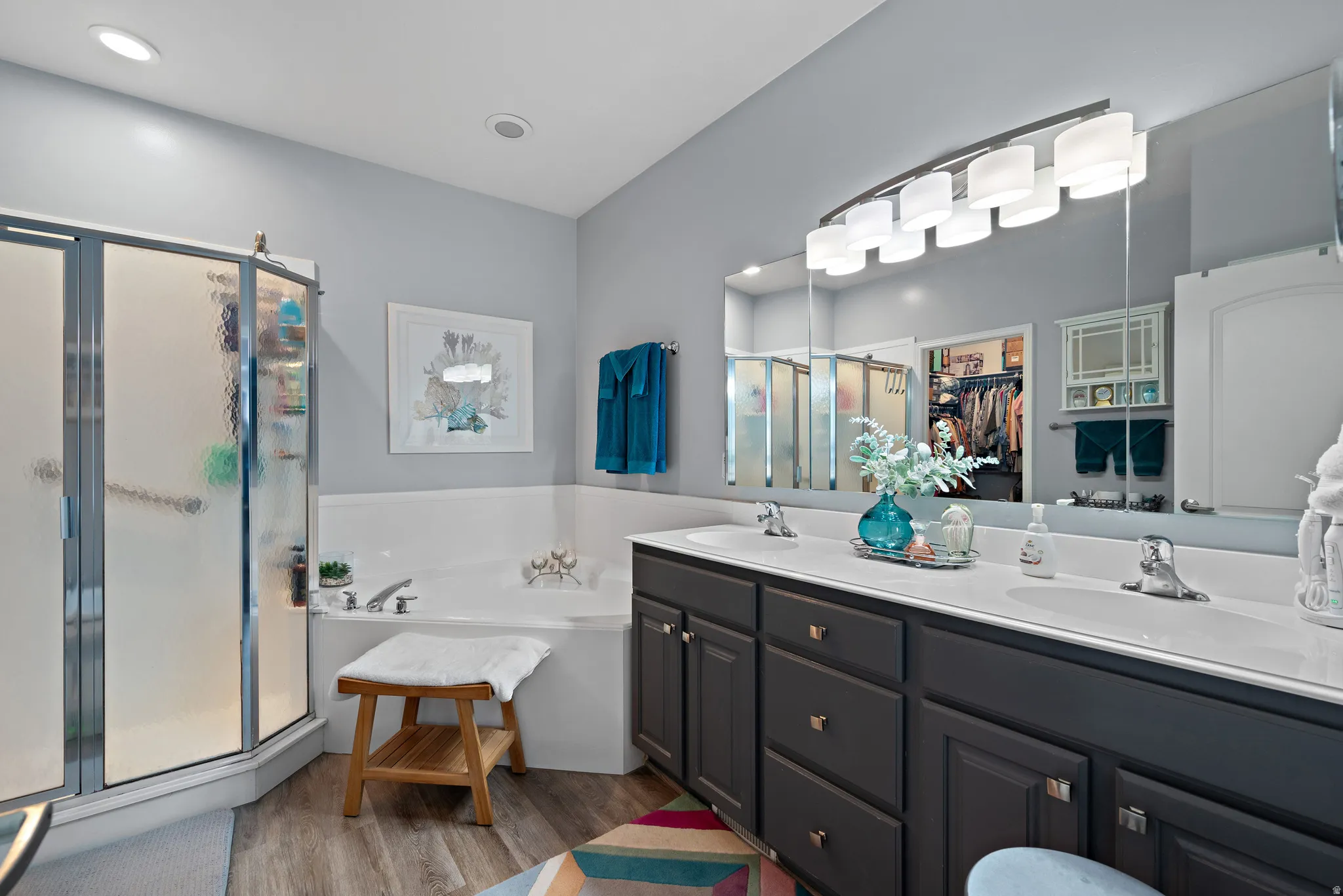 Full bath featuring a walk in closet, double vanity, a stall shower, a garden tub, and light wood-style flooring