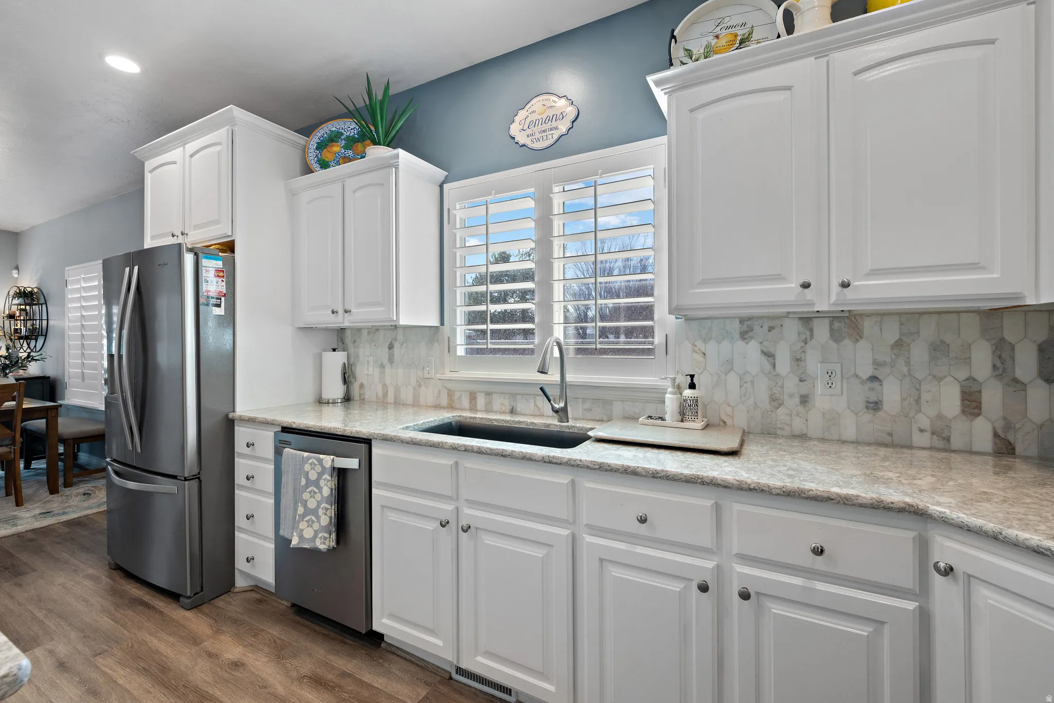 Kitchen with white cabinetry, stainless steel appliances, backsplash, light stone counters, and dark wood-style floors