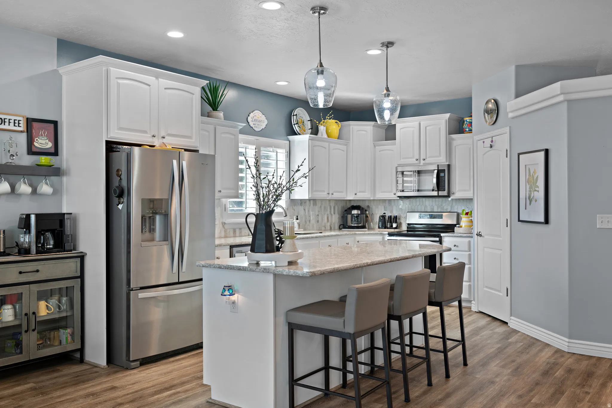 Kitchen with light stone countertops, a kitchen bar, stainless steel appliances, white cabinetry, and a kitchen island