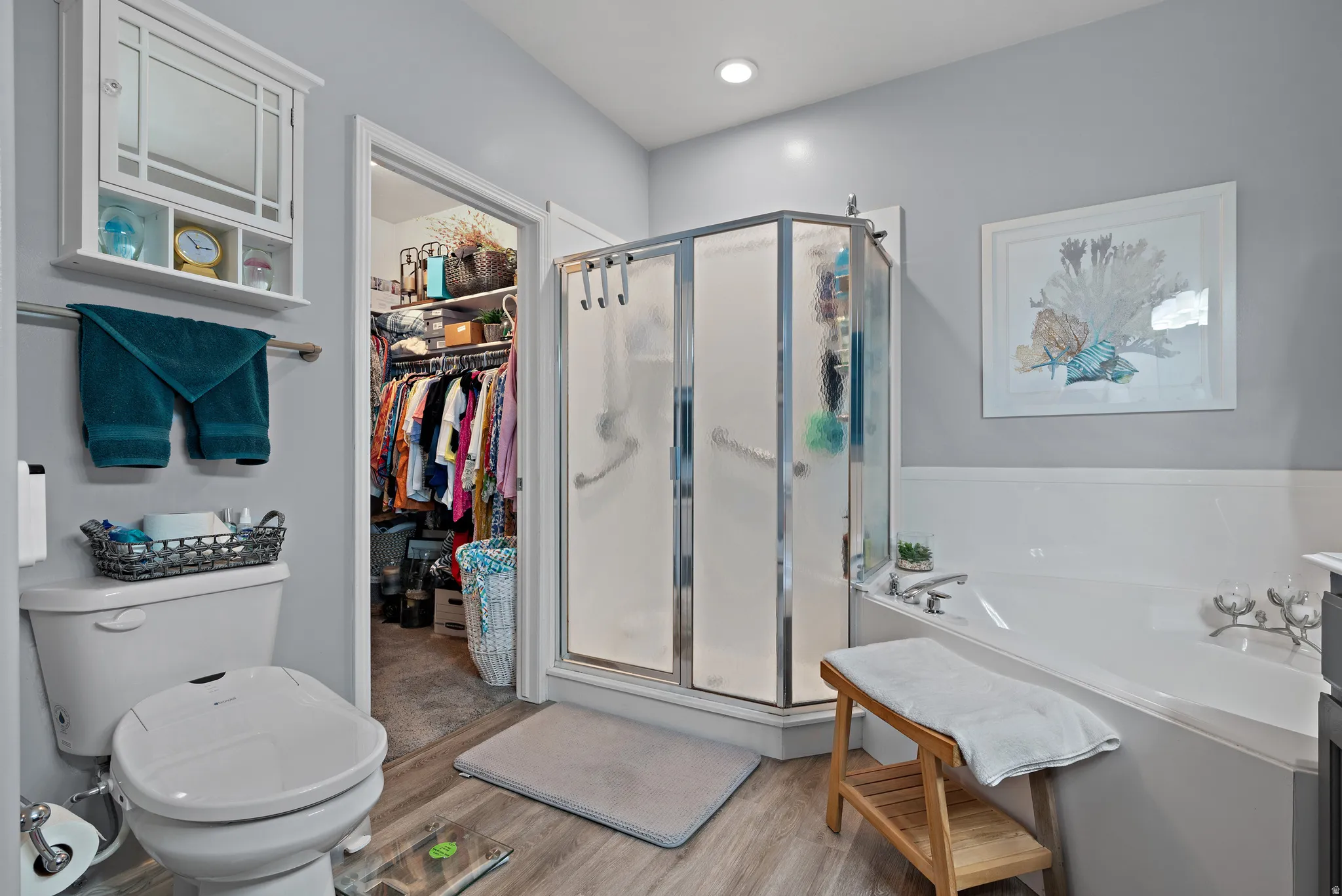 Bathroom featuring a shower stall, light wood-style floors, a garden tub, and a spacious closet