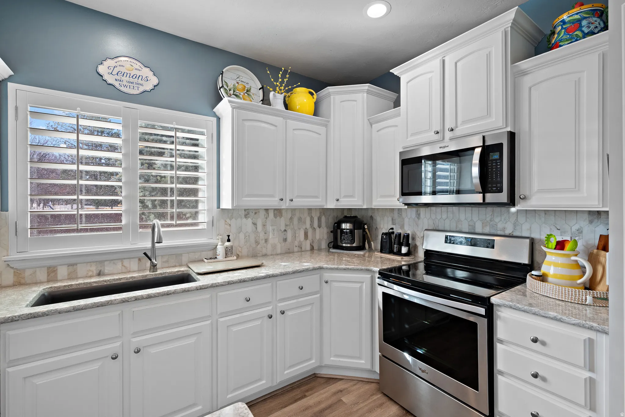 Kitchen with stainless steel appliances, white cabinetry, light stone counters, decorative backsplash, and light wood-style floors