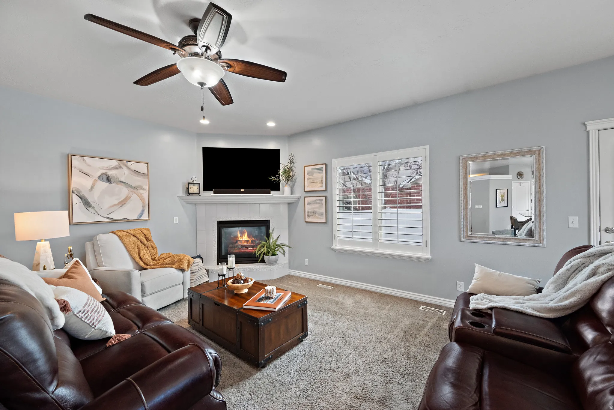 Carpeted living area with a ceiling fan, a tile fireplace, and recessed lighting
