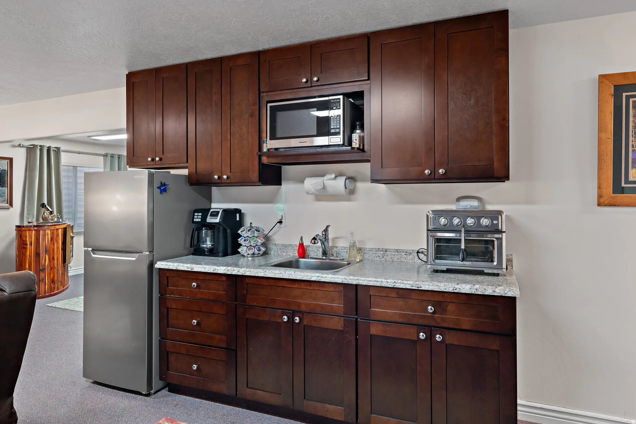 Kitchen featuring stainless steel appliances, light stone counters, dark wood finish cabinetry, a textured ceiling, and dark carpet