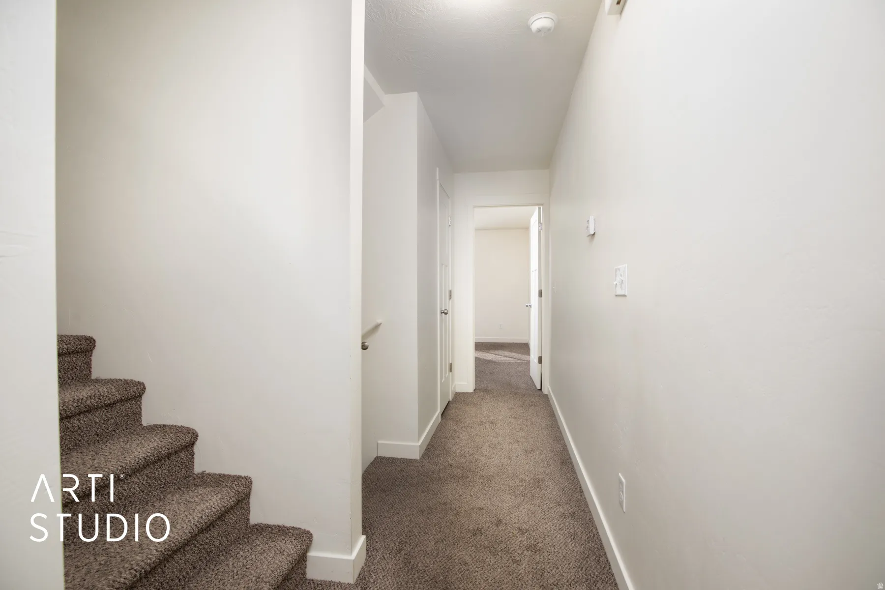 Hallway with dark carpet and baseboards leading to primary bedroom.