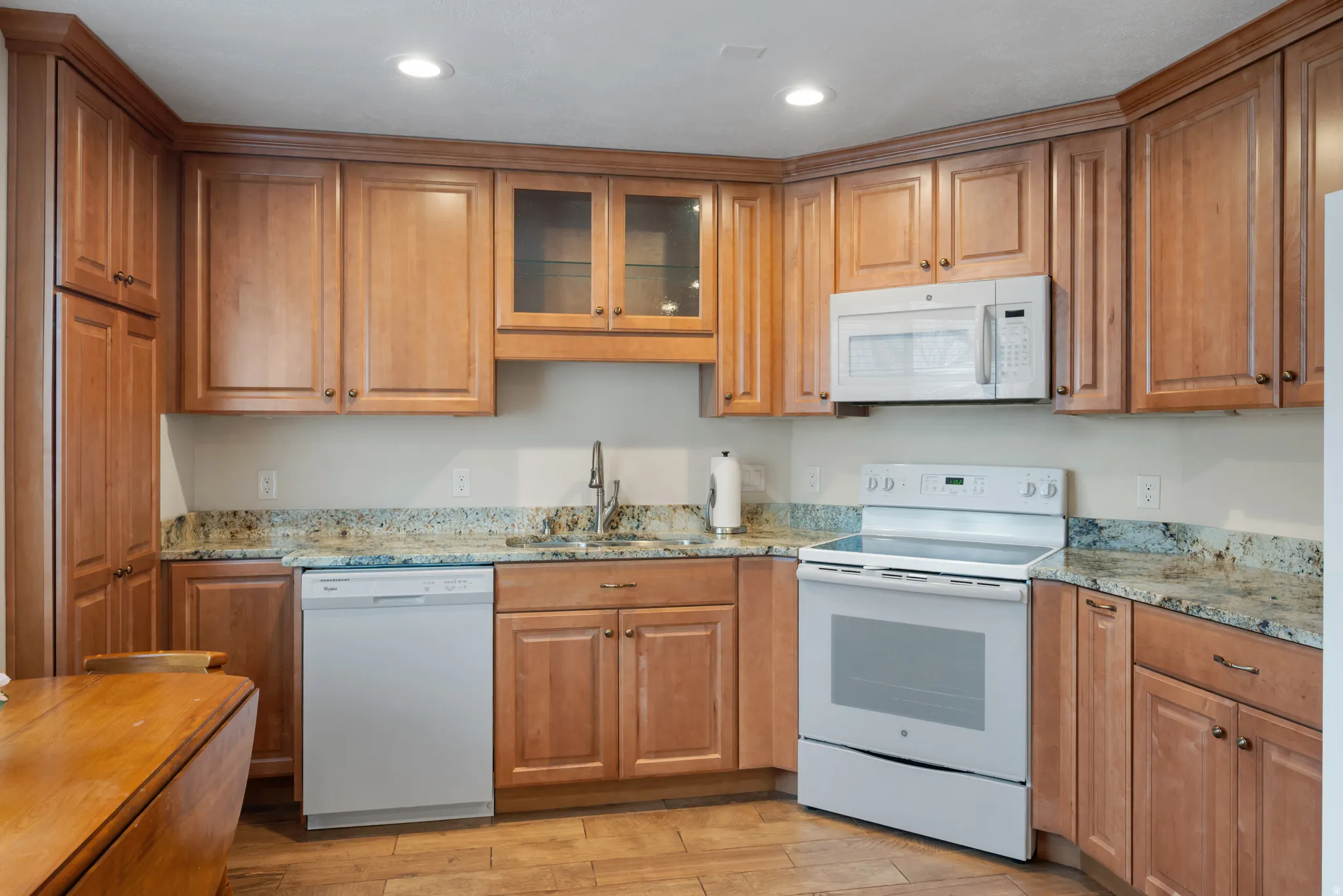 Full Kitchen with white appliances, glass insert cabinets, light stone countertops, wood finish cabinetry, and recessed lighting