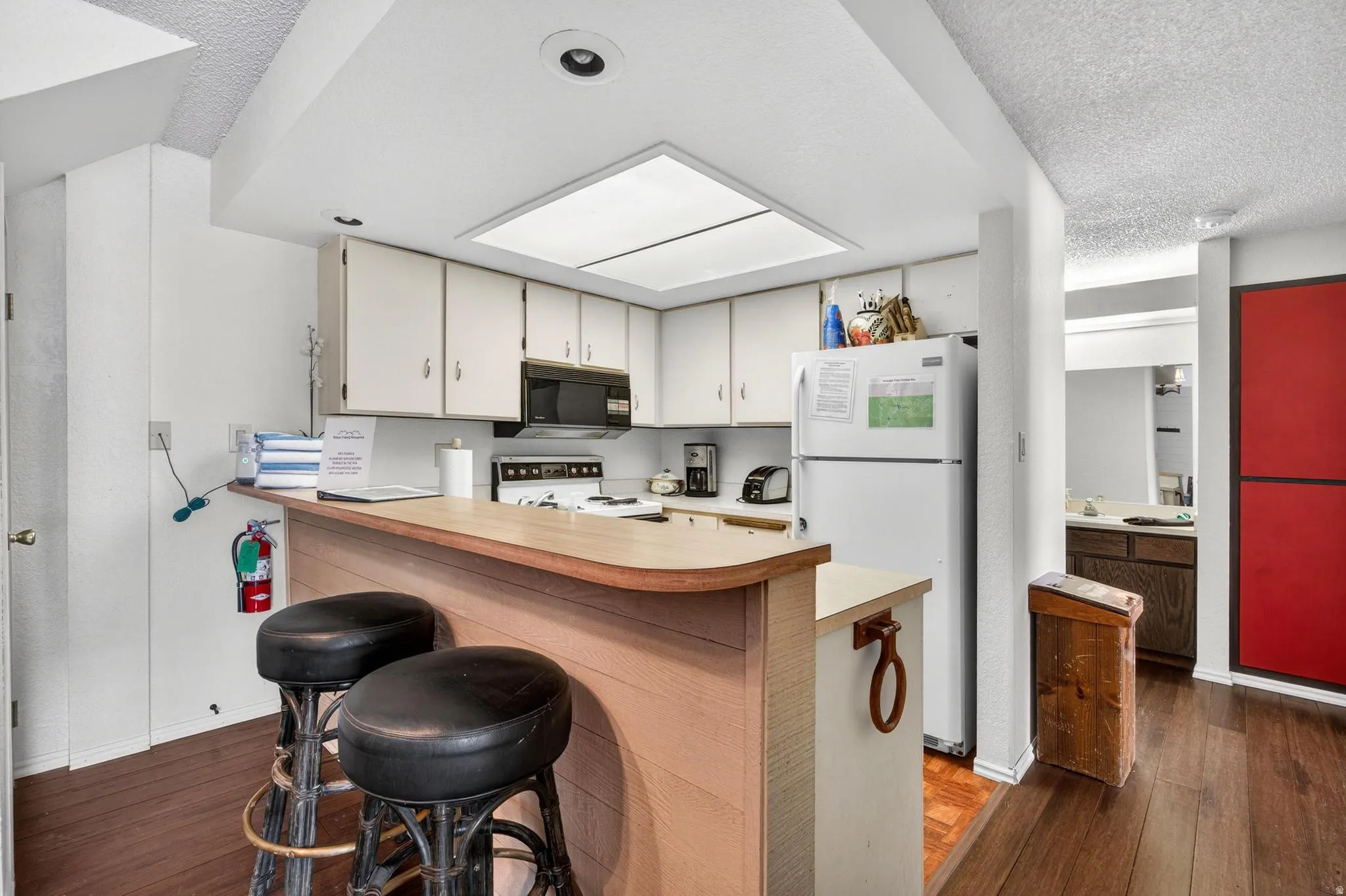 Kitchen featuring light countertops, a breakfast bar area, white appliances, dark wood-style floors, and a textured ceiling