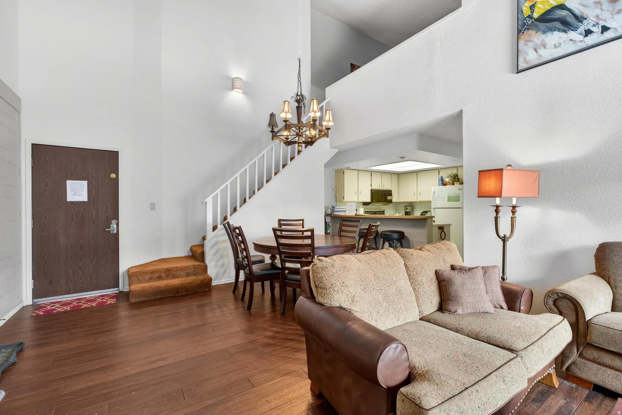Living room with suspended lighting, dark wood-style floors, and a high ceiling