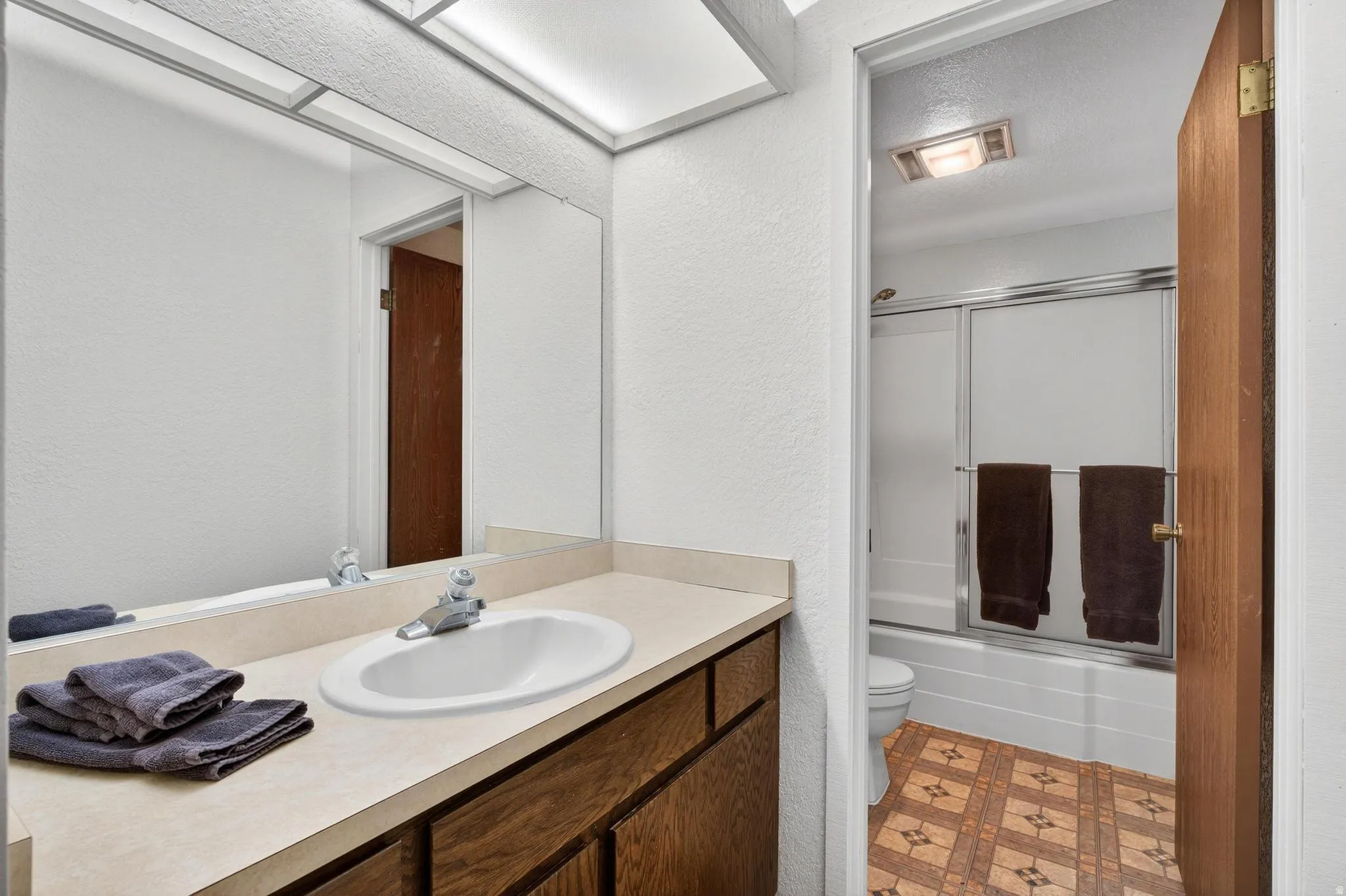 Bathroom with combined bath / shower with glass door, a textured wall, vanity, light flooring, and a textured ceiling