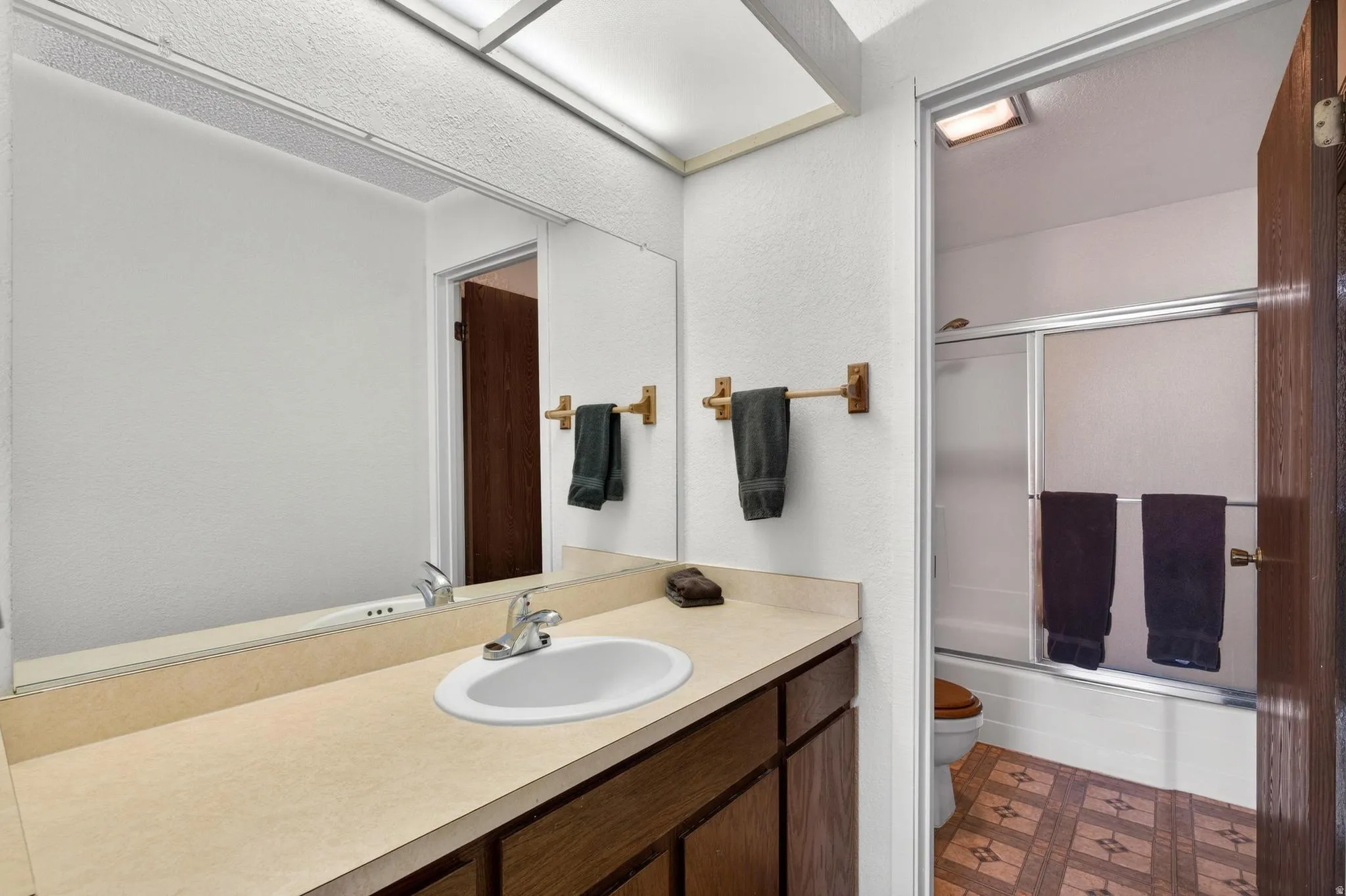 Full bathroom featuring bath / shower combo with glass door, vanity, dark floors, and a textured wall