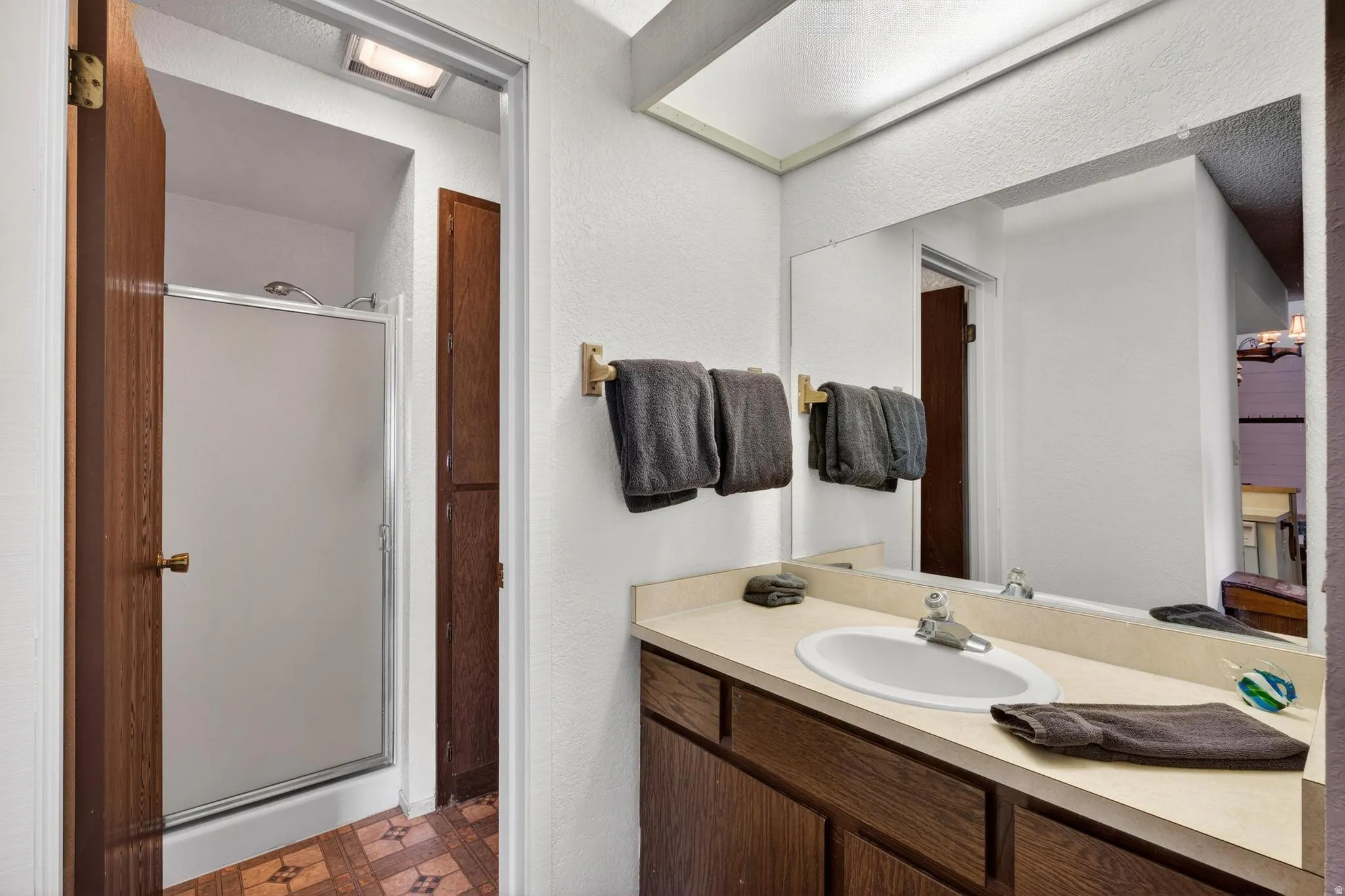 Full bath featuring vanity, a stall shower, dark floors, and a textured wall