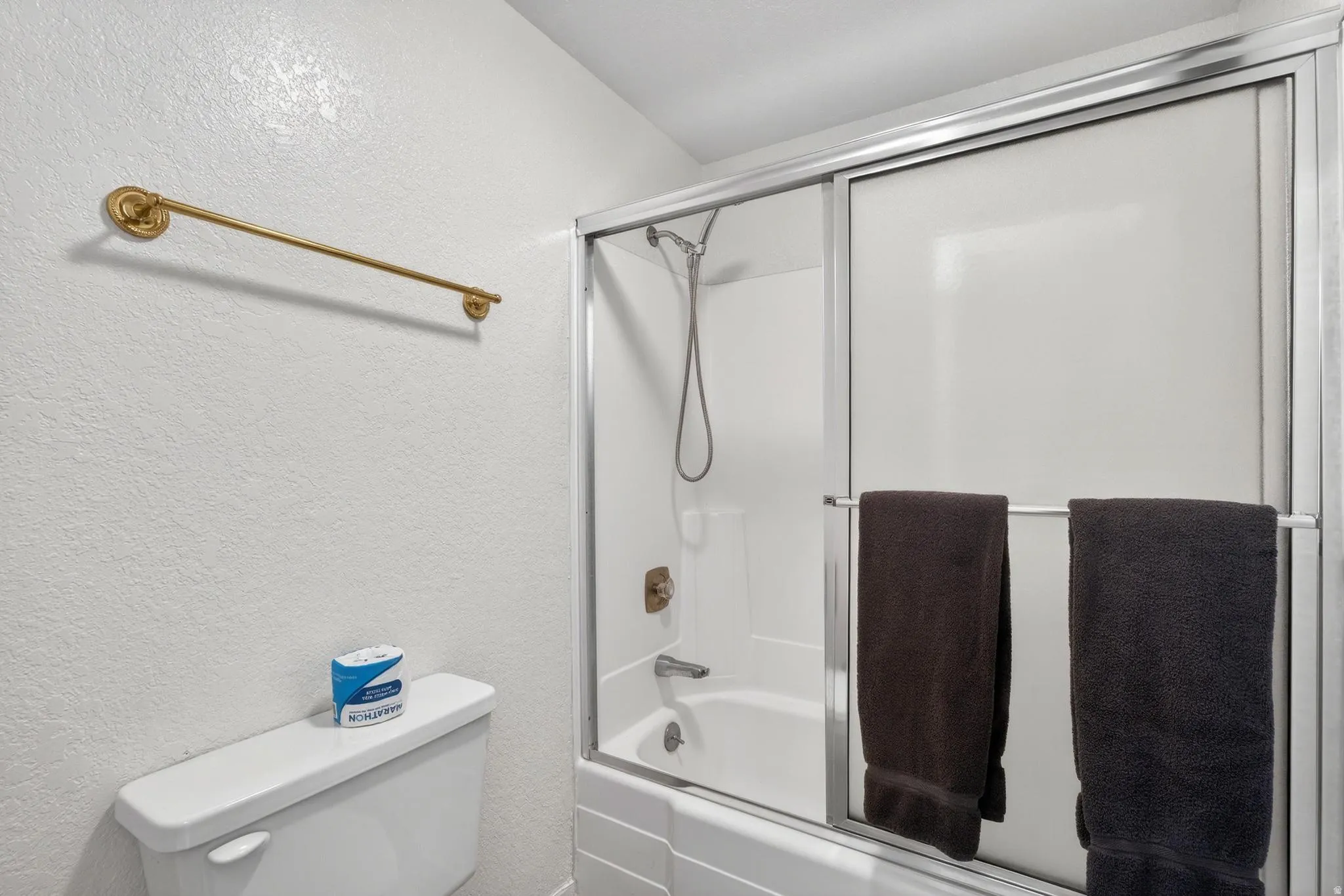 Bathroom with a textured wall and enclosed tub / shower combo