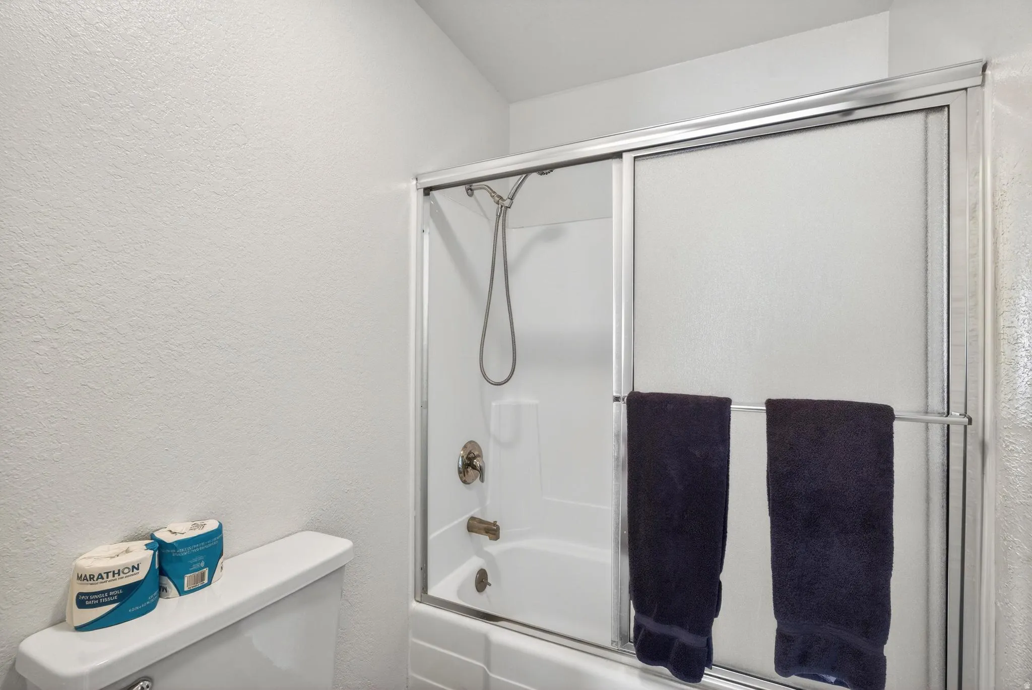 Full bath with a textured wall and combined bath / shower with glass door