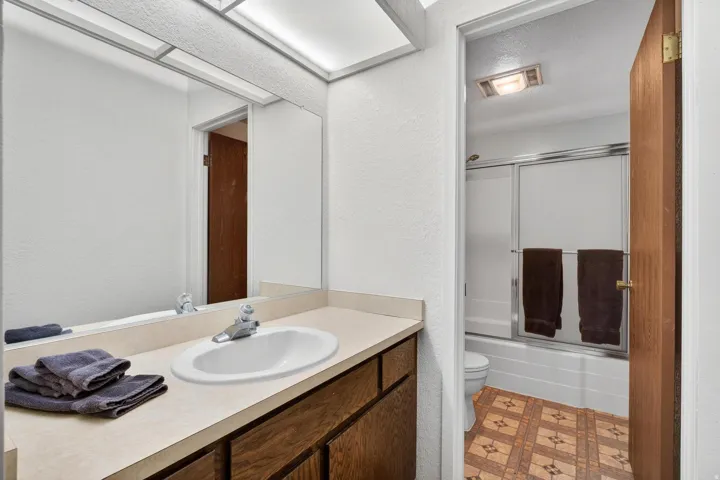 Bathroom with combined bath / shower with glass door, a textured wall, vanity, light flooring, and a textured ceiling