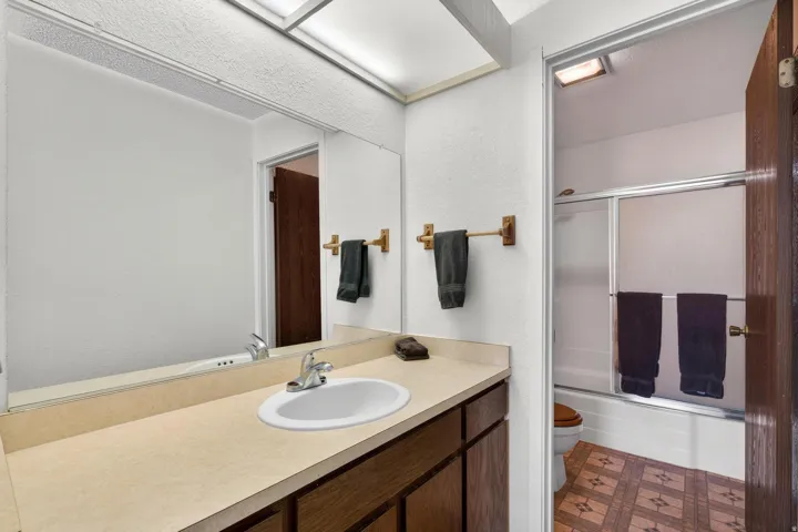 Full bathroom featuring bath / shower combo with glass door, vanity, dark floors, and a textured wall