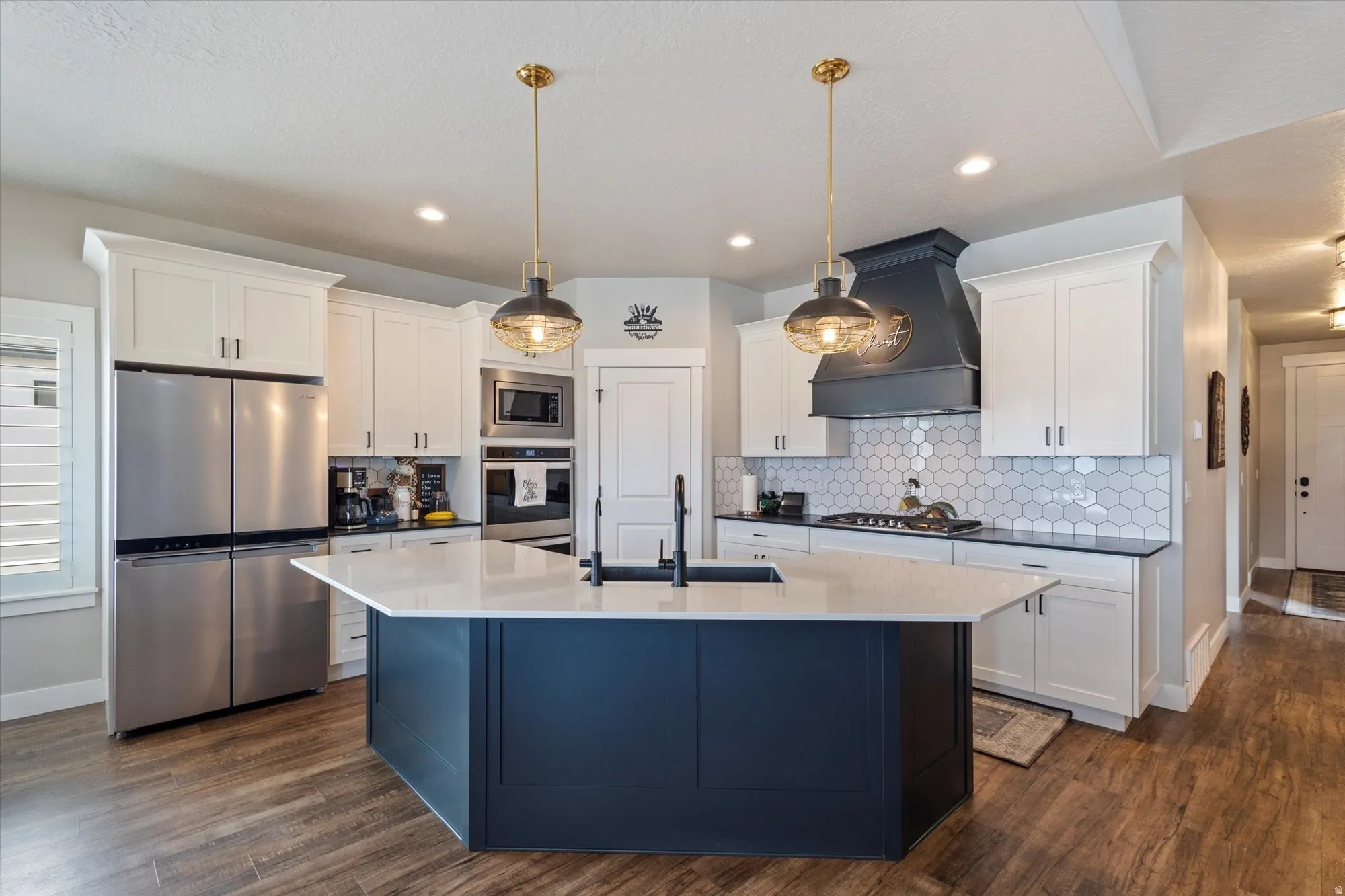 Dual tone kitchen with dual tone cabinets, stainless steel appliances, a center island with sink, decorative light fixtures, and dark wood finished floors