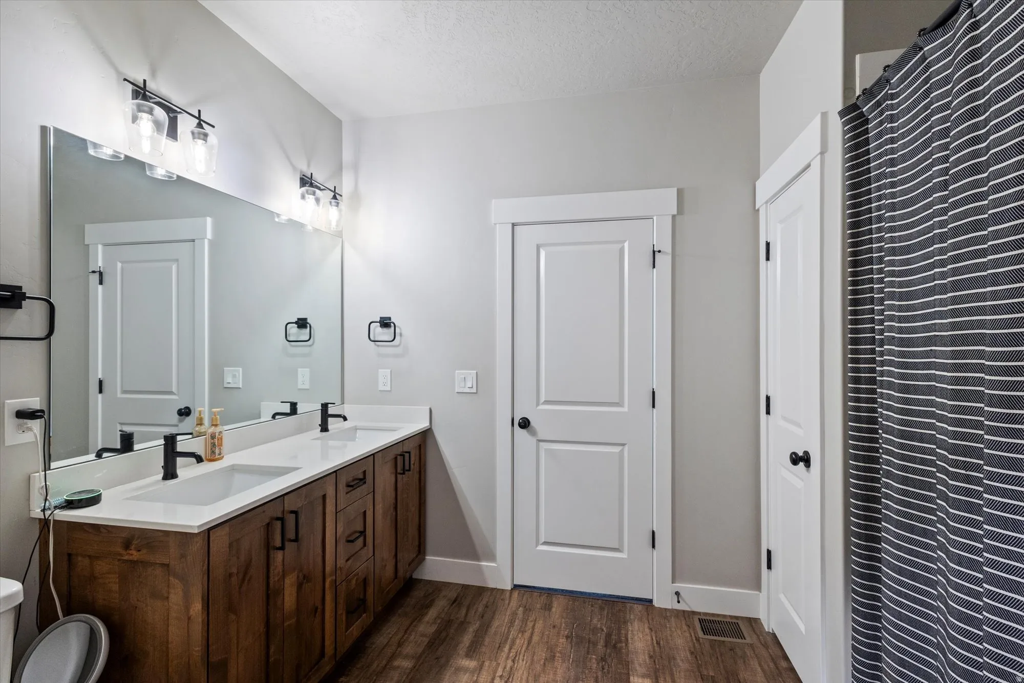 Full bath featuring double vanity, dark wood-style floors, and a textured ceiling