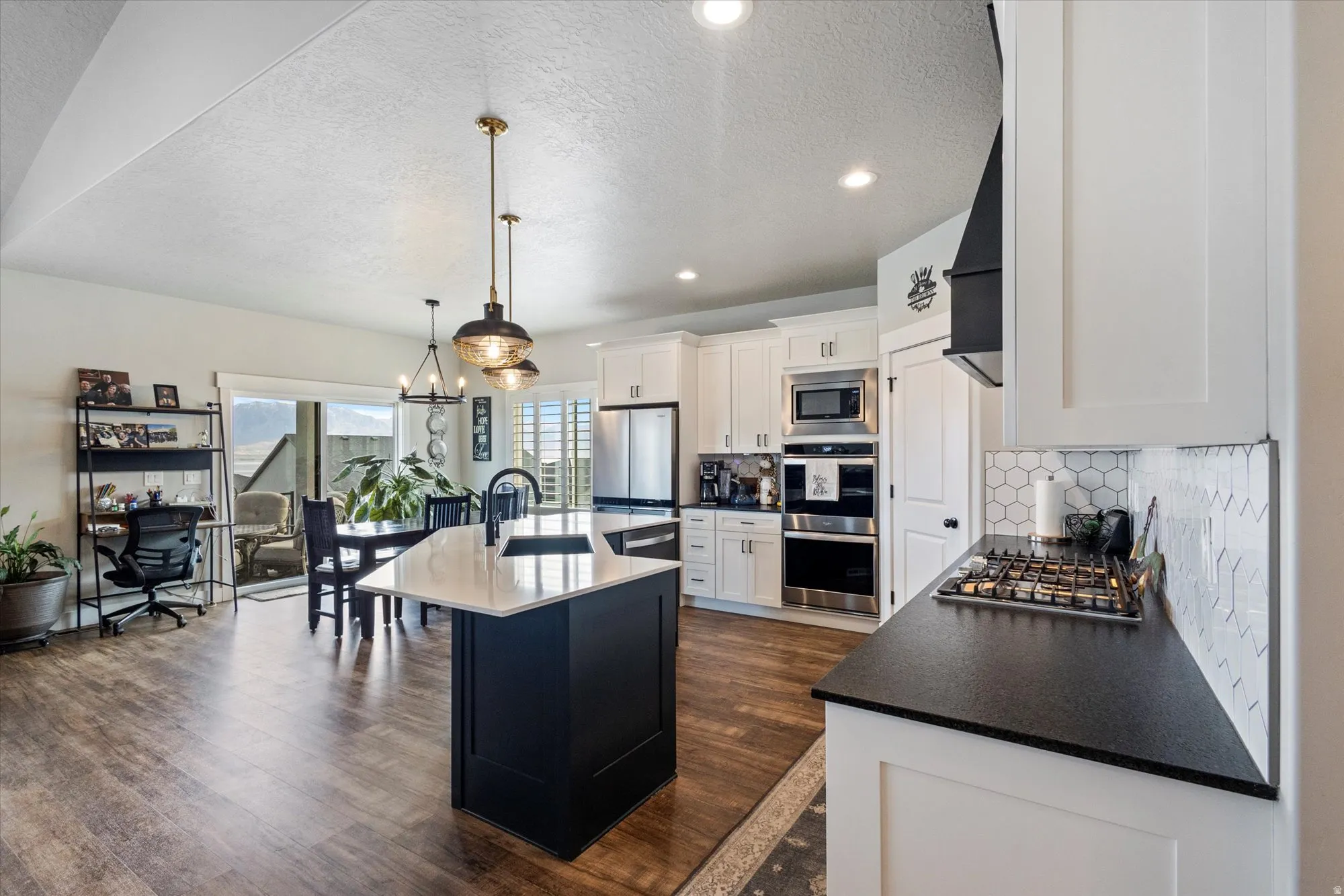 Kitchen with a textured ceiling, a center island with sink, stainless steel appliances, dark wood-type flooring, and a chandelier