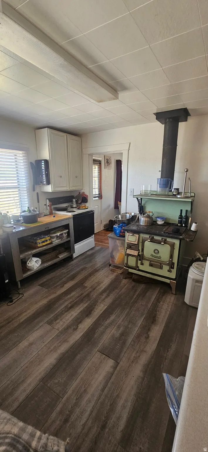 Kitchen featuring dark wood finished floors, healthy amount of natural light, white range with electric stovetop, and a wood stove