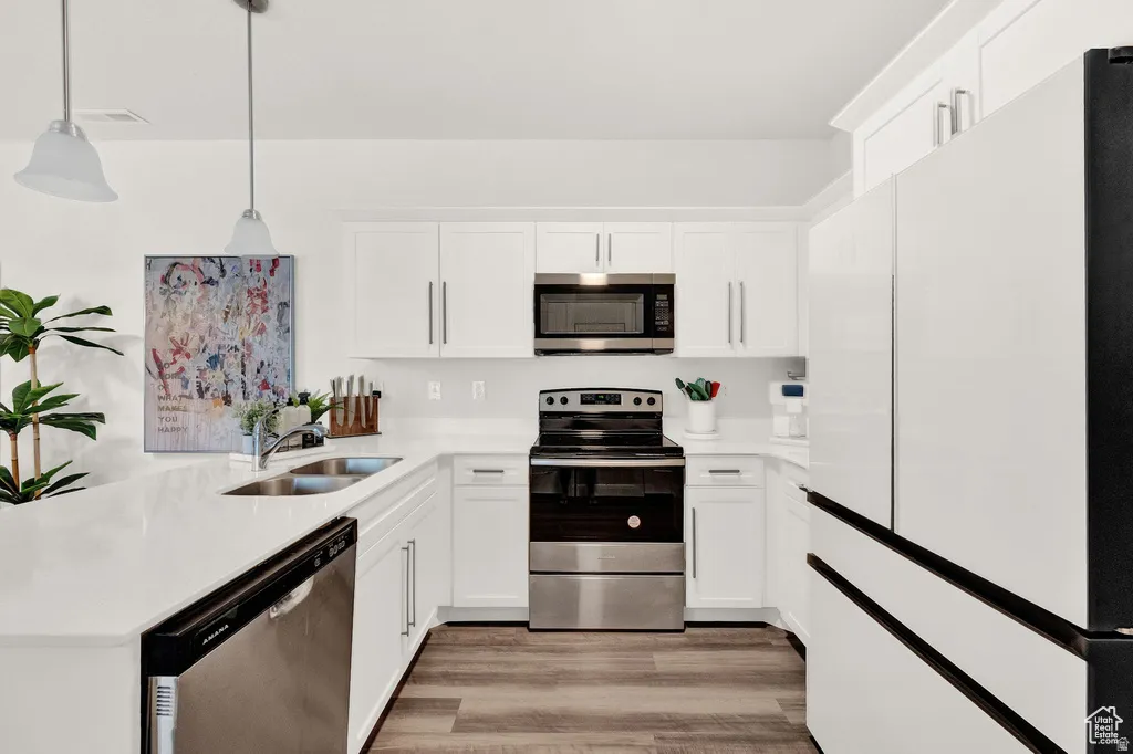 Kitchen featuring stainless steel appliances, white cabinetry, a peninsula, and pendant lighting