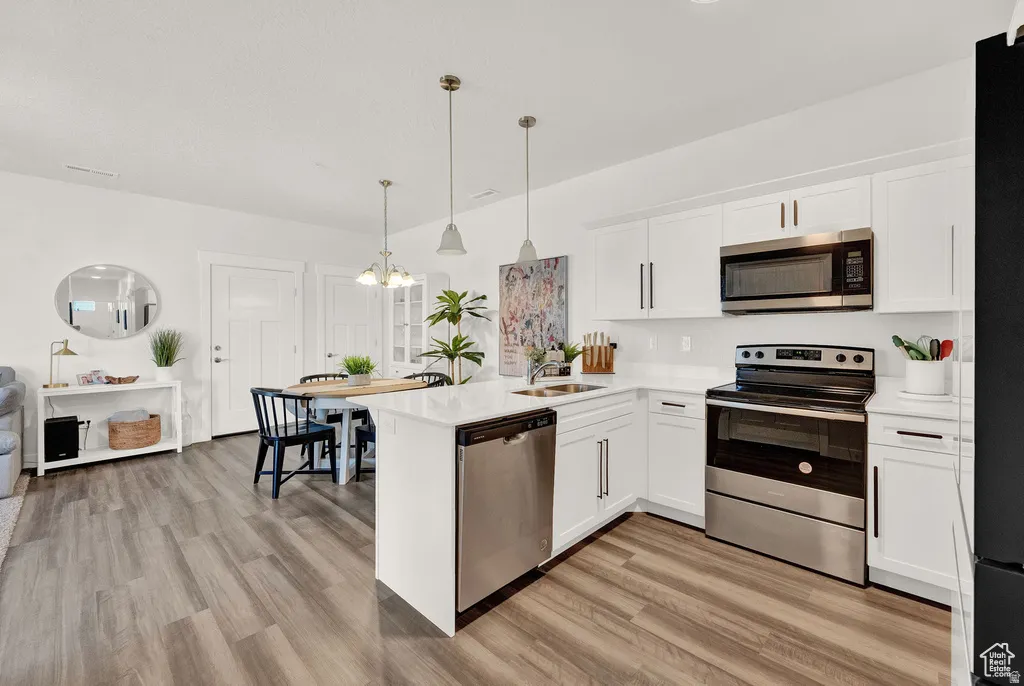 Kitchen with stainless steel appliances, white cabinetry, a peninsula, and light wood-style floors