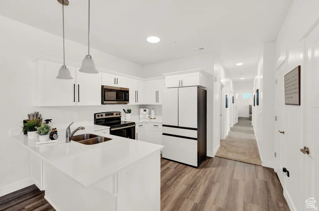 Kitchen featuring stainless steel appliances, hanging light fixtures, white cabinets, and a peninsula