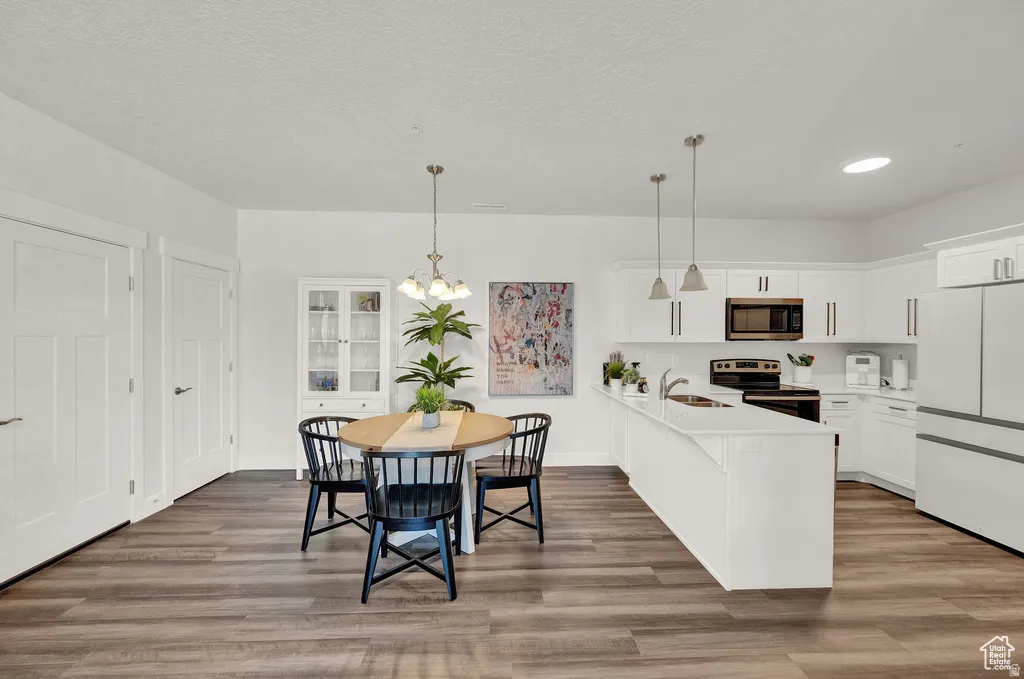 Kitchen with a peninsula, stainless steel appliances, white cabinetry, dark wood-style floors, and a textured ceiling