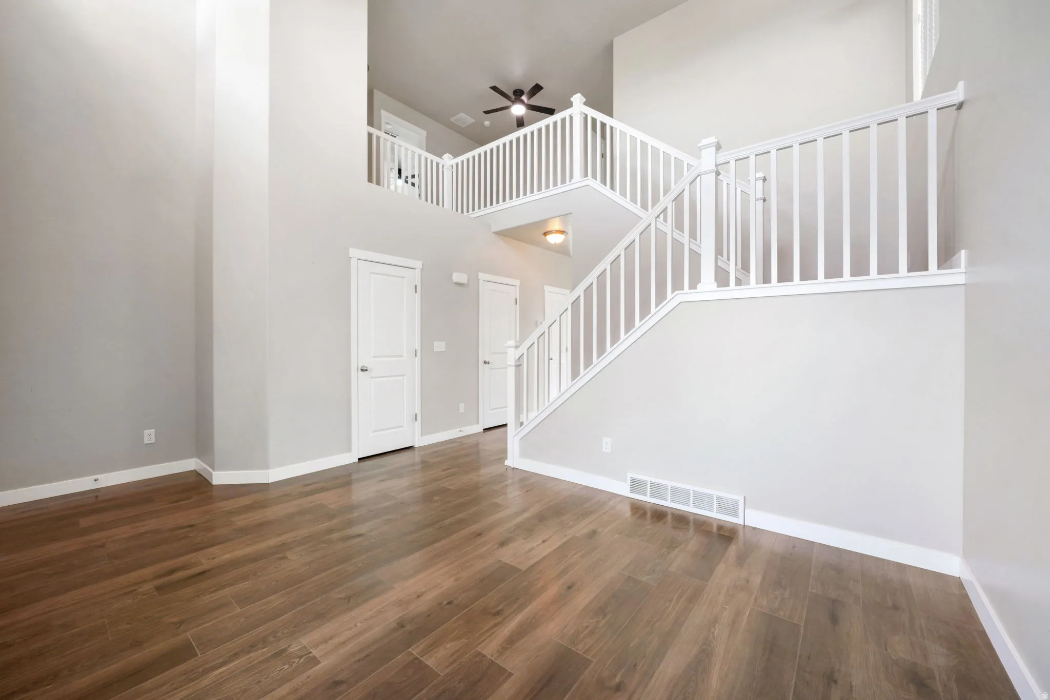 Unfurnished living room featuring ceiling fan, dark wood-style flooring, and a high ceiling
