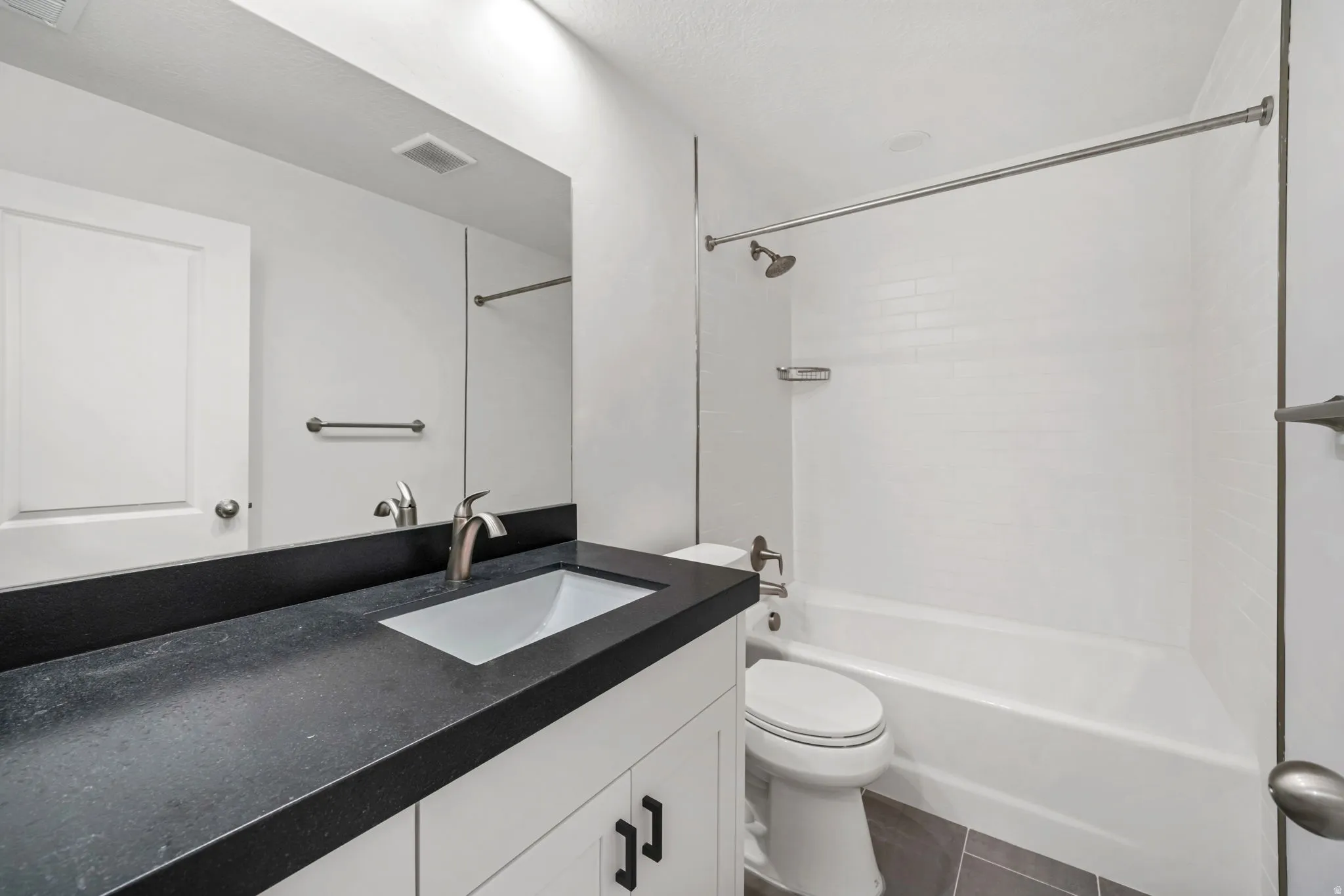 Bathroom with vanity, tub / shower combination, and dark tile patterned flooring