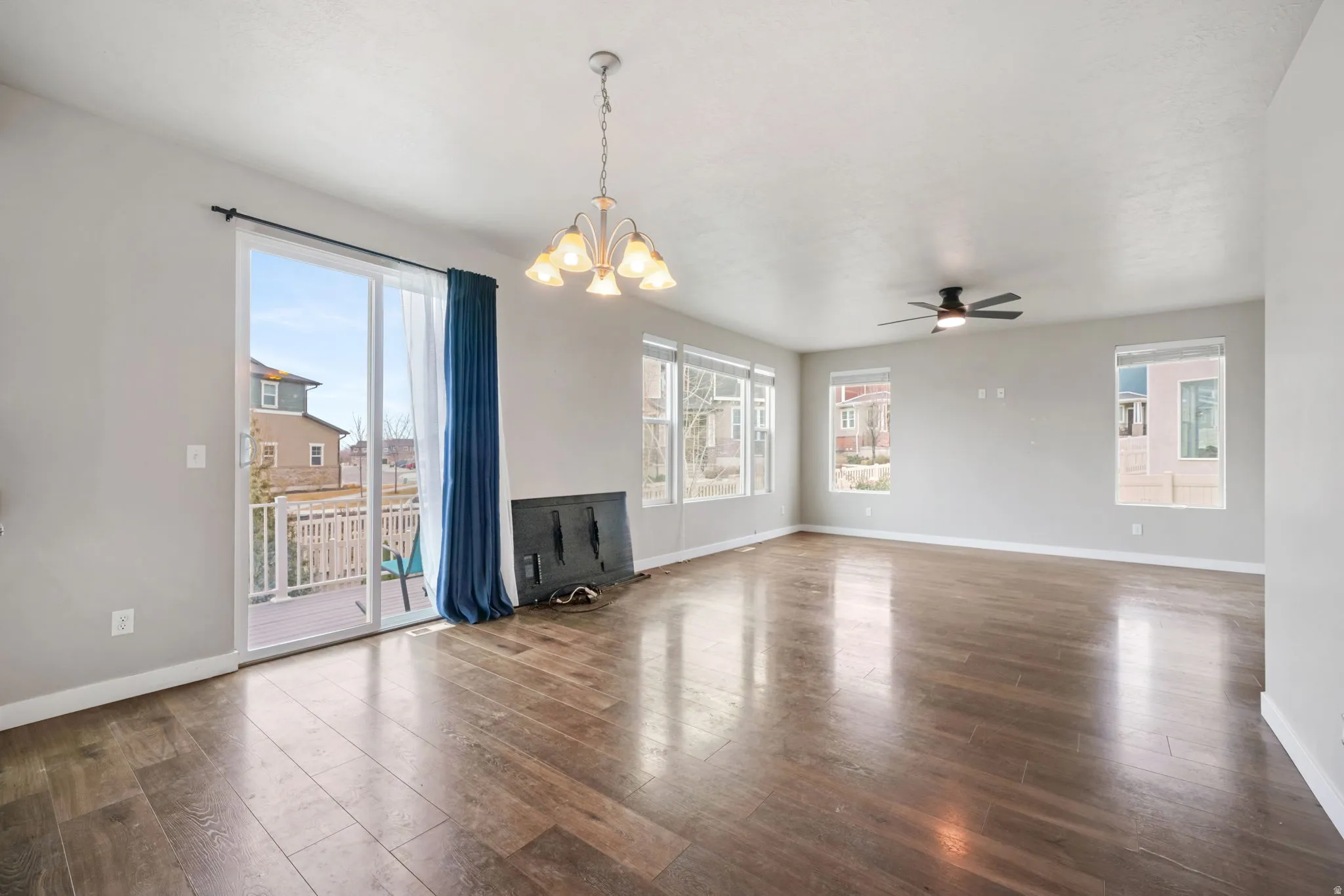 Unfurnished living room with hanging lights, a ceiling fan, dark wood-style flooring, and healthy amount of natural light