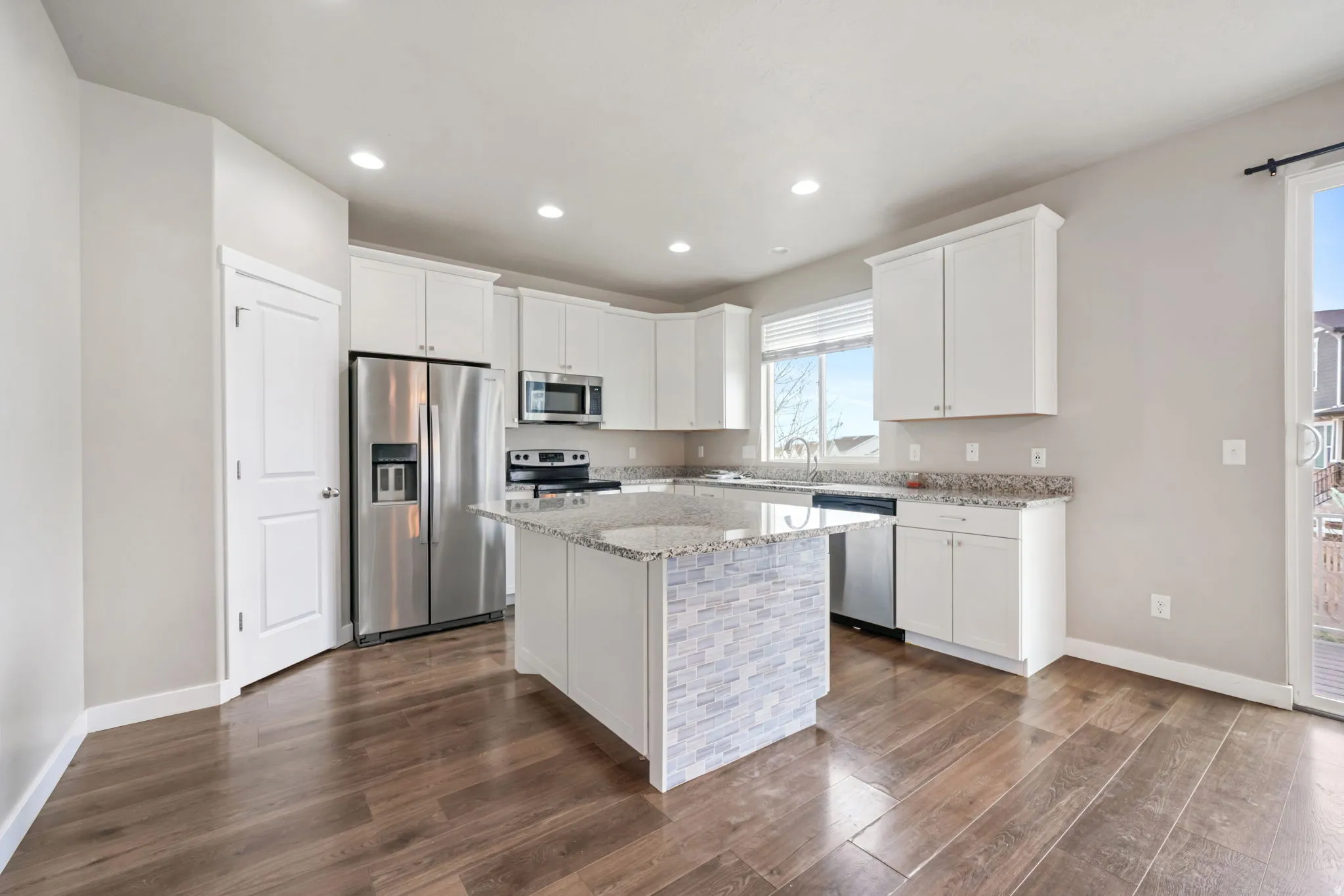 Kitchen featuring stainless steel appliances, white cabinets, light stone counters, dark wood-style floors, and recessed lighting