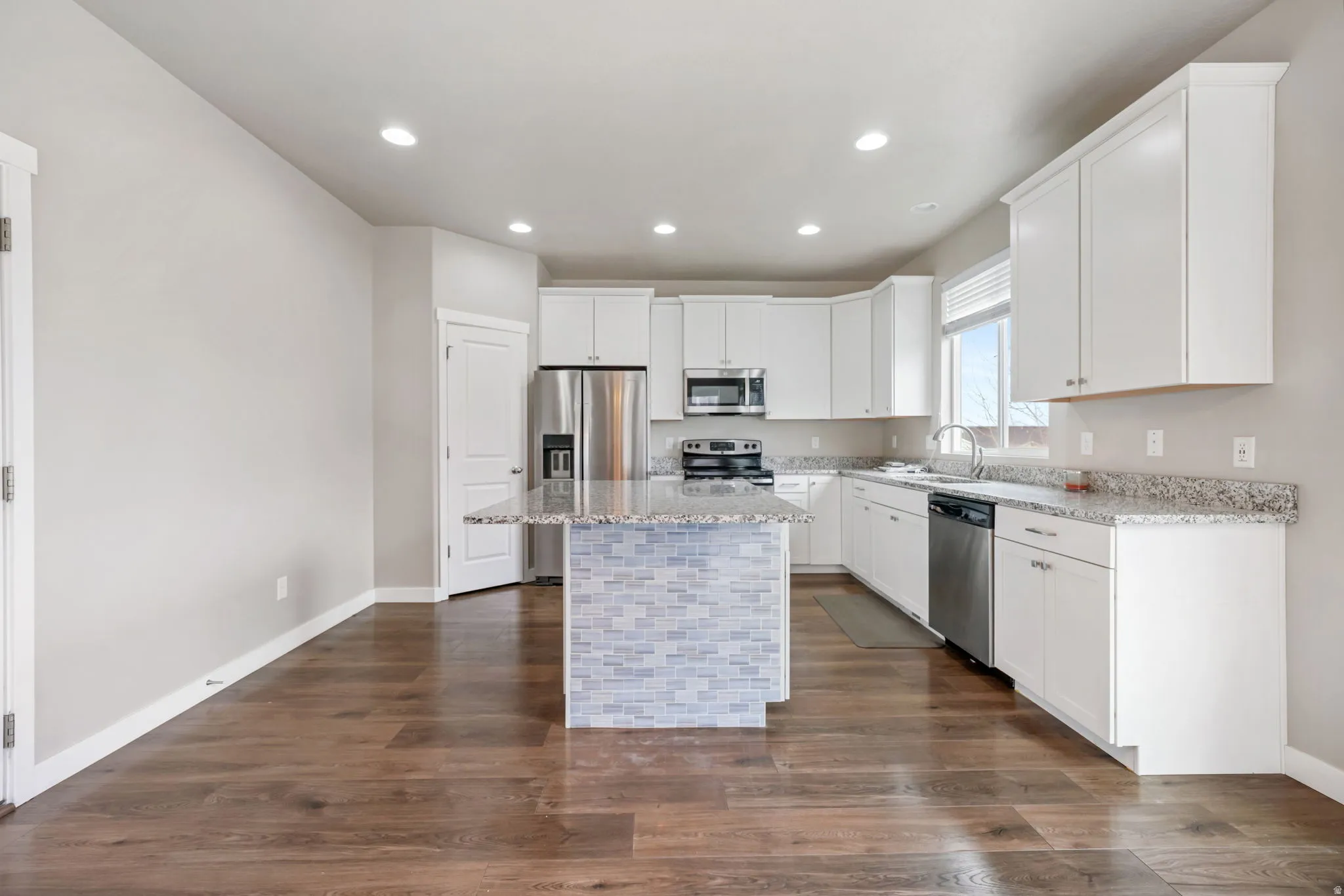 Kitchen with white cabinetry, light stone countertops, a kitchen island, stainless steel appliances, and dark wood finished floors