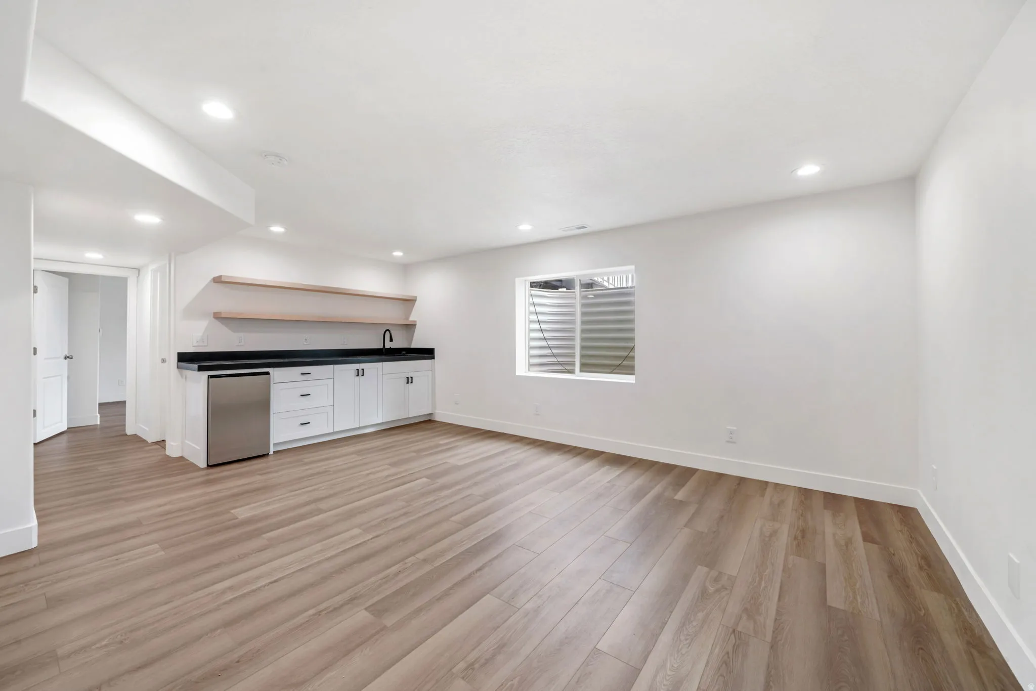 Kitchen featuring open shelves, light wood-type flooring, dark countertops, white cabinetry, and stainless steel refrigerator