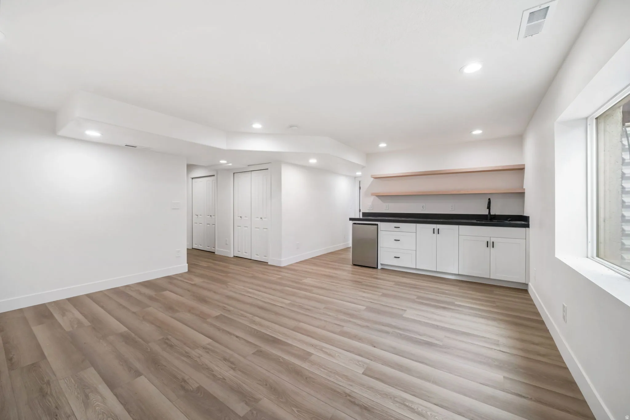 Indoor wet bar featuring open shelves, white cabinetry, light wood-type flooring, dark countertops, and recessed lighting