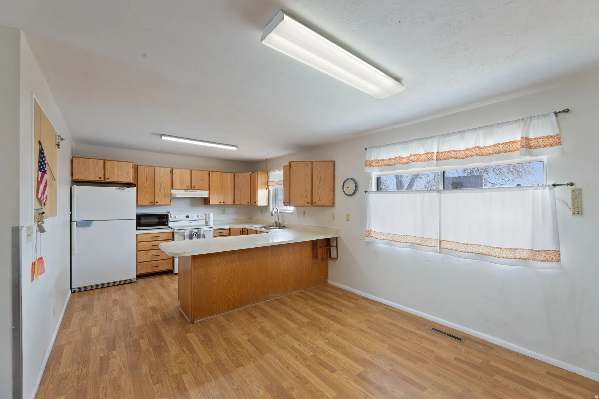 Kitchen with light countertops, white appliances, a peninsula, and light wood-type flooring