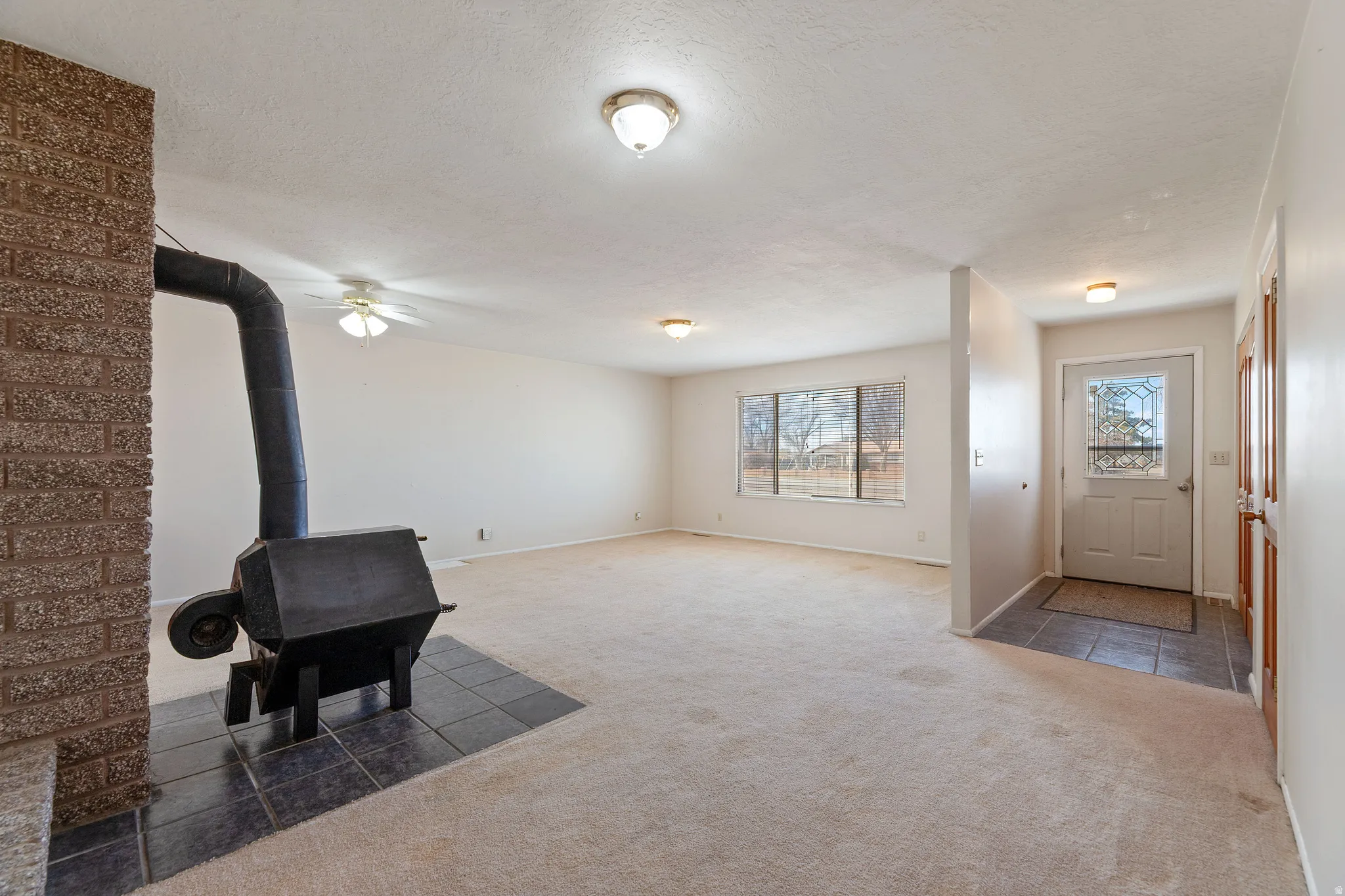Carpeted entryway featuring a wood stove, a textured ceiling, tile patterned floors, and a ceiling fan
