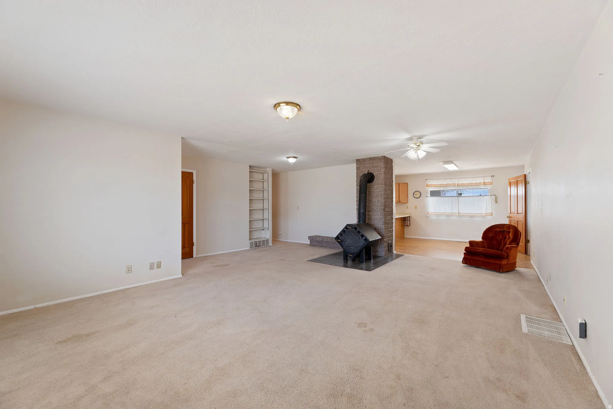 Unfurnished room featuring a wood stove, light carpet, and ceiling fan
