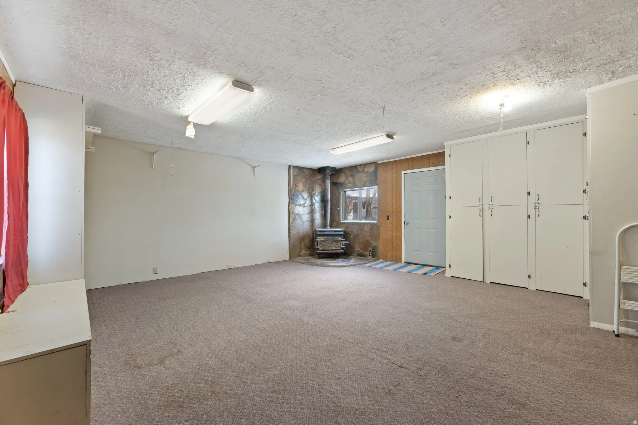 Below grade area featuring a wood stove, carpet floors, a textured ceiling, and wooden walls