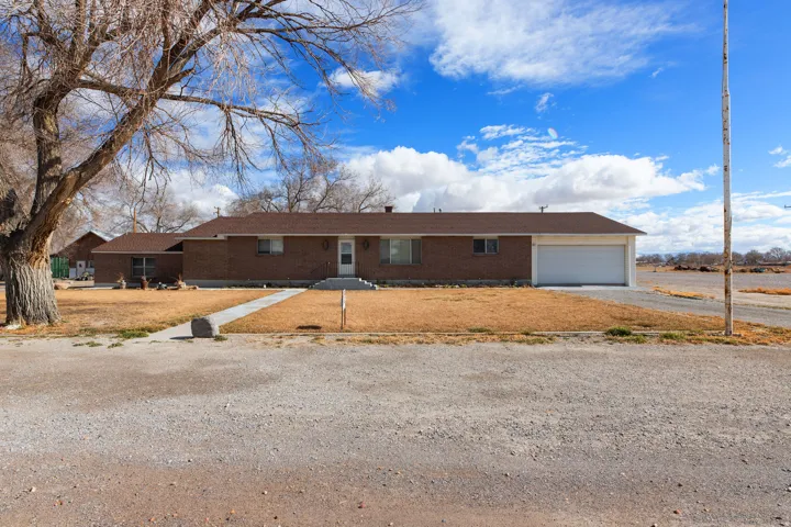 Single story home with brick siding, gravel driveway, a garage, and a front lawn