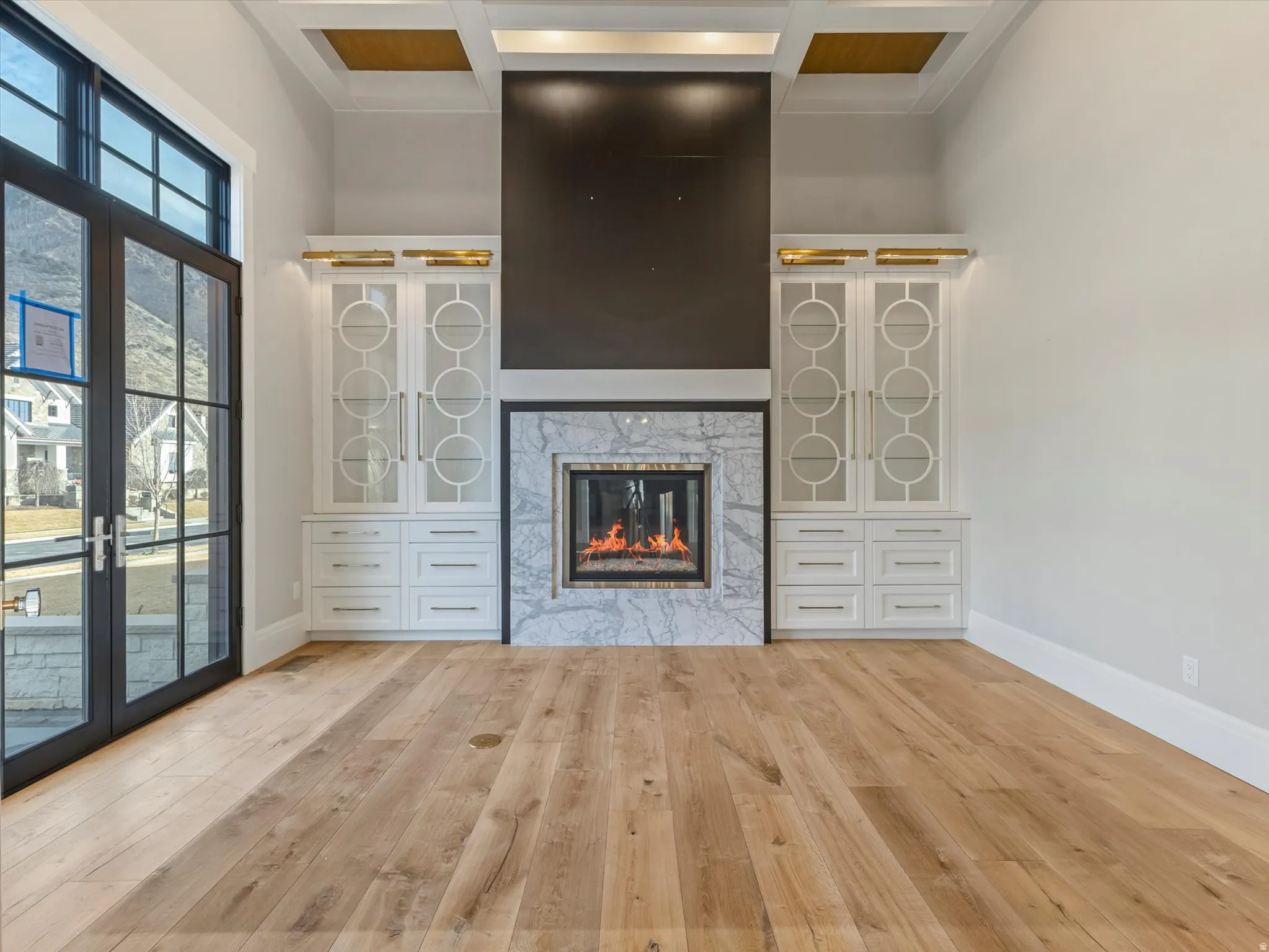 Unfurnished living room with coffered ceiling, a high end fireplace, and light wood-style flooring