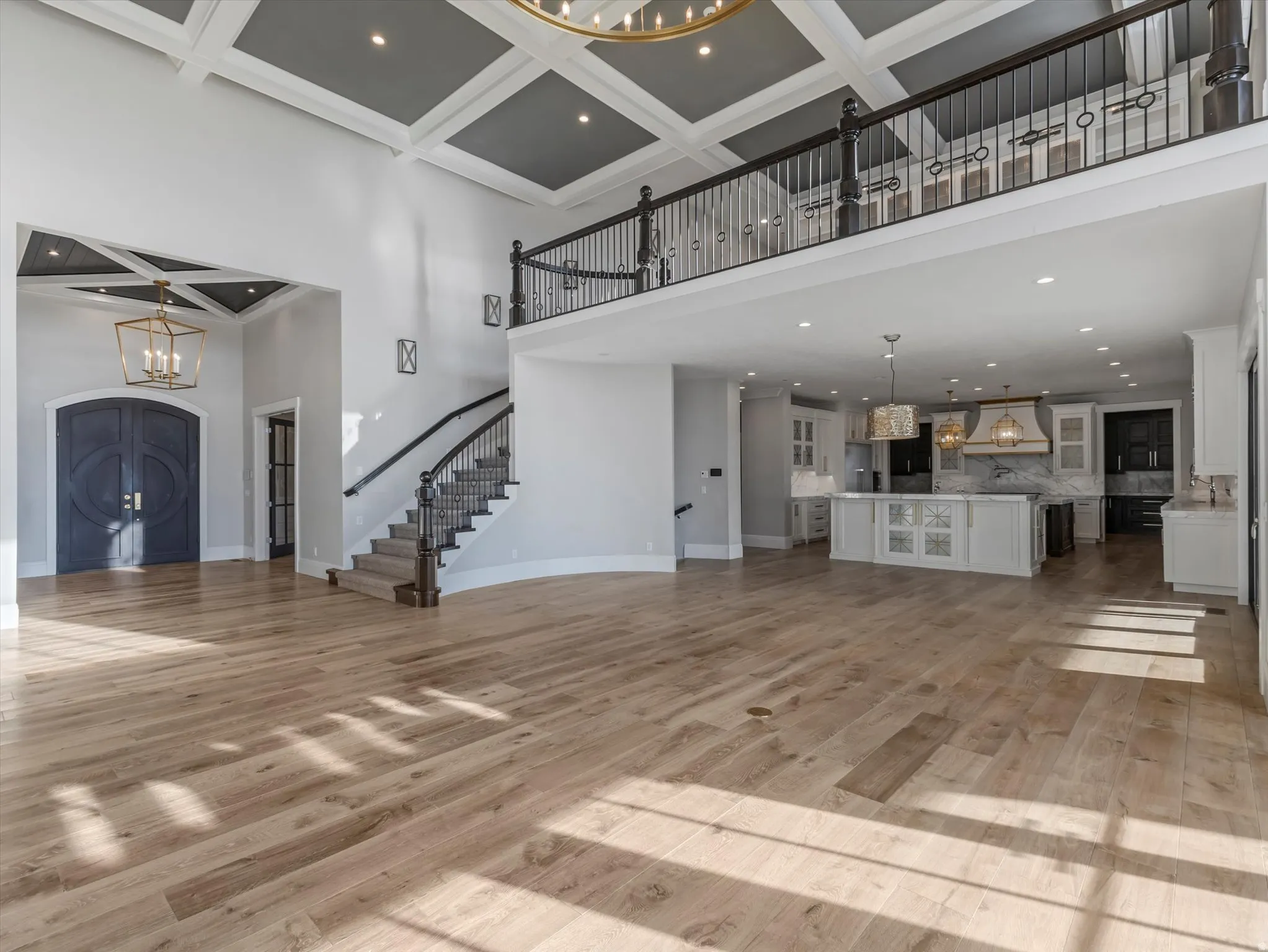 Unfurnished living room with hanging lights, coffered ceiling, ornamental molding, and light wood-style floors