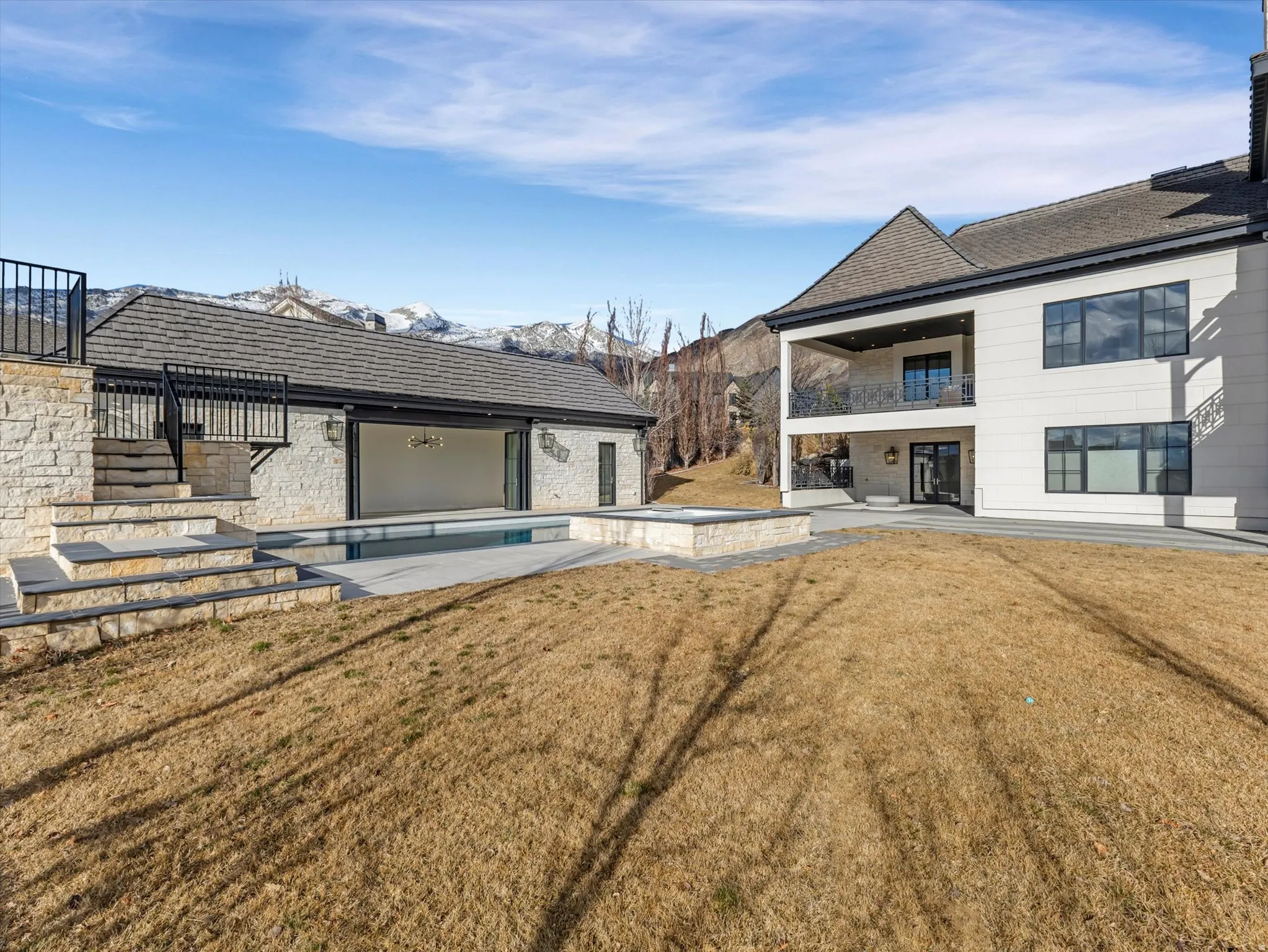 Rear view of house with a patio, a lawn, a balcony, a pool with connected hot tub, and a mountain view