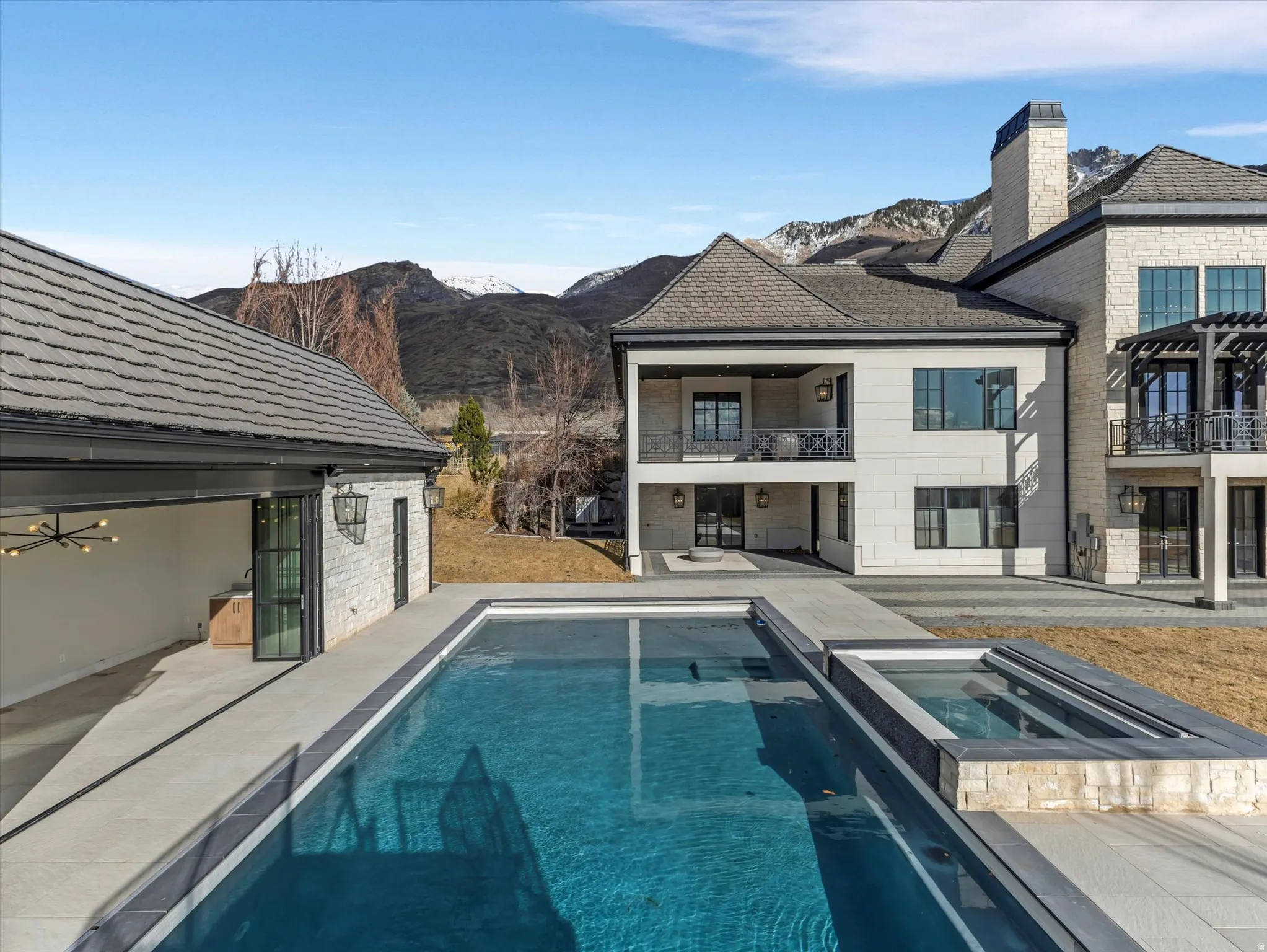 Back of house with open air Casita, patio, a pool with connected hot tub, a mountain view, a balcony, and stone siding