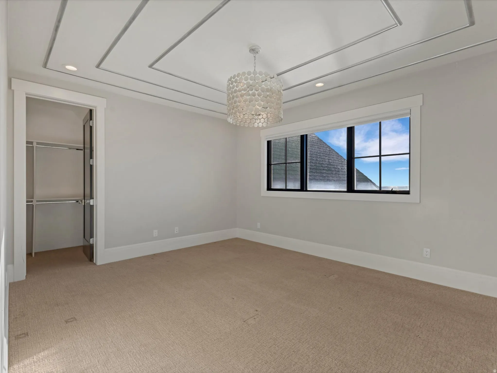 Unfurnished bedroom with light carpet, suspended lighting, and a walk in closet