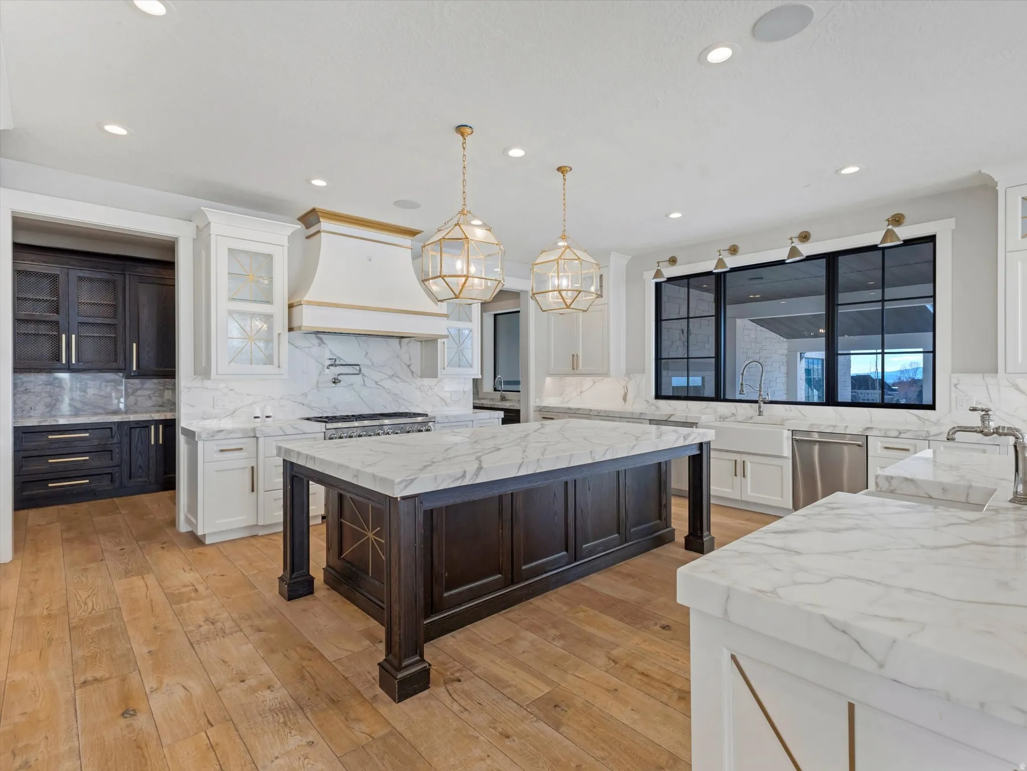 Kitchen with two tone color scheme, light stone counters, backsplash, decorative light fixtures, and light wood-style flooring