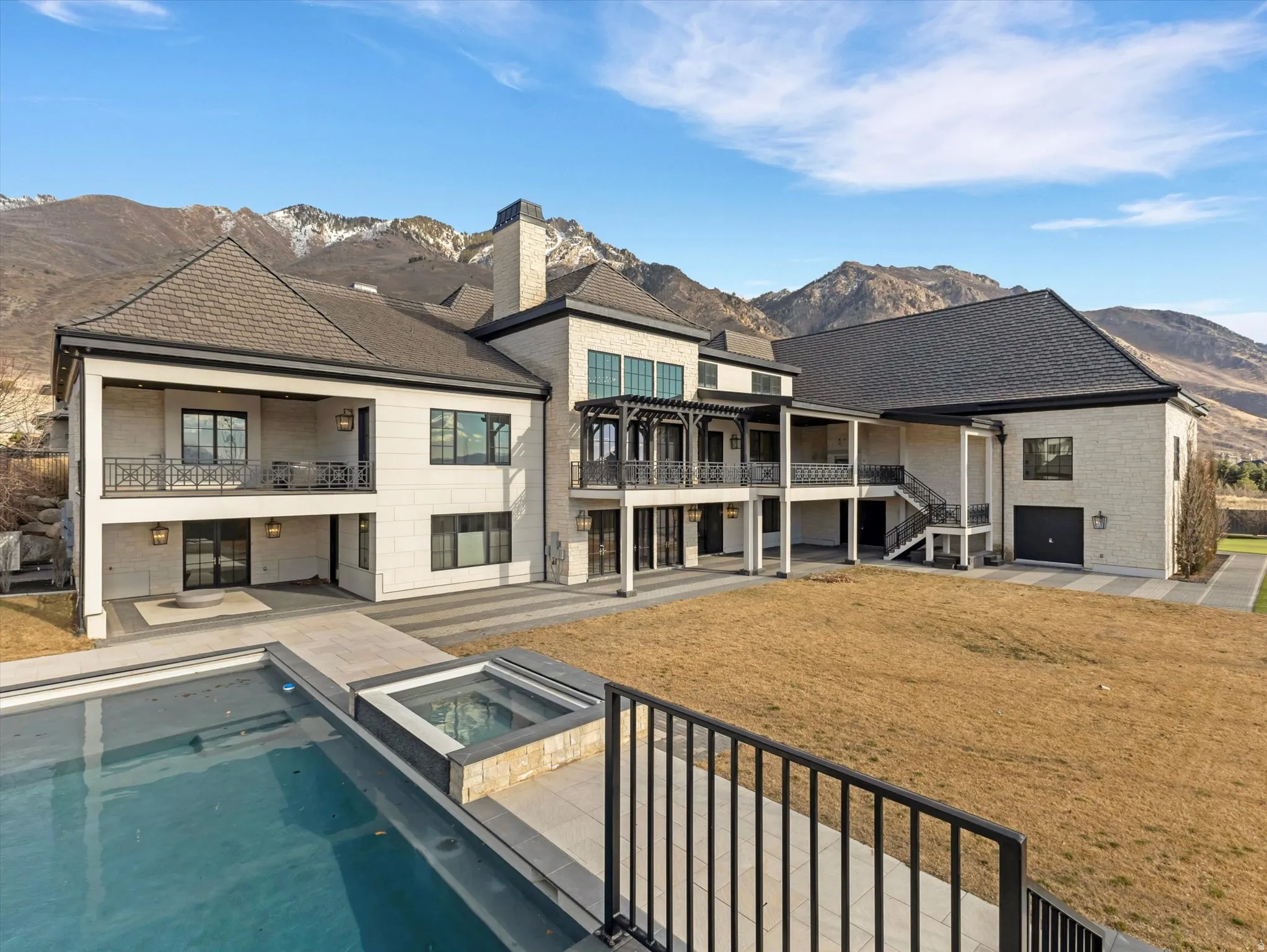 Back of house with a patio area, a mountain view, a balcony, a pool with connected hot tub, and stone siding