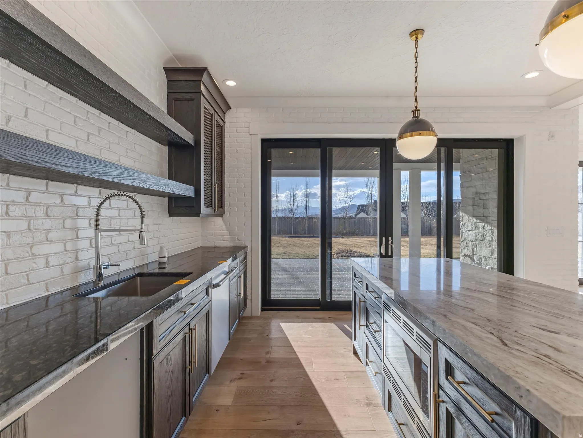 Kitchen featuring dark stone counters, open shelves, pendant lighting, light wood-style floors, and stainless steel appliances