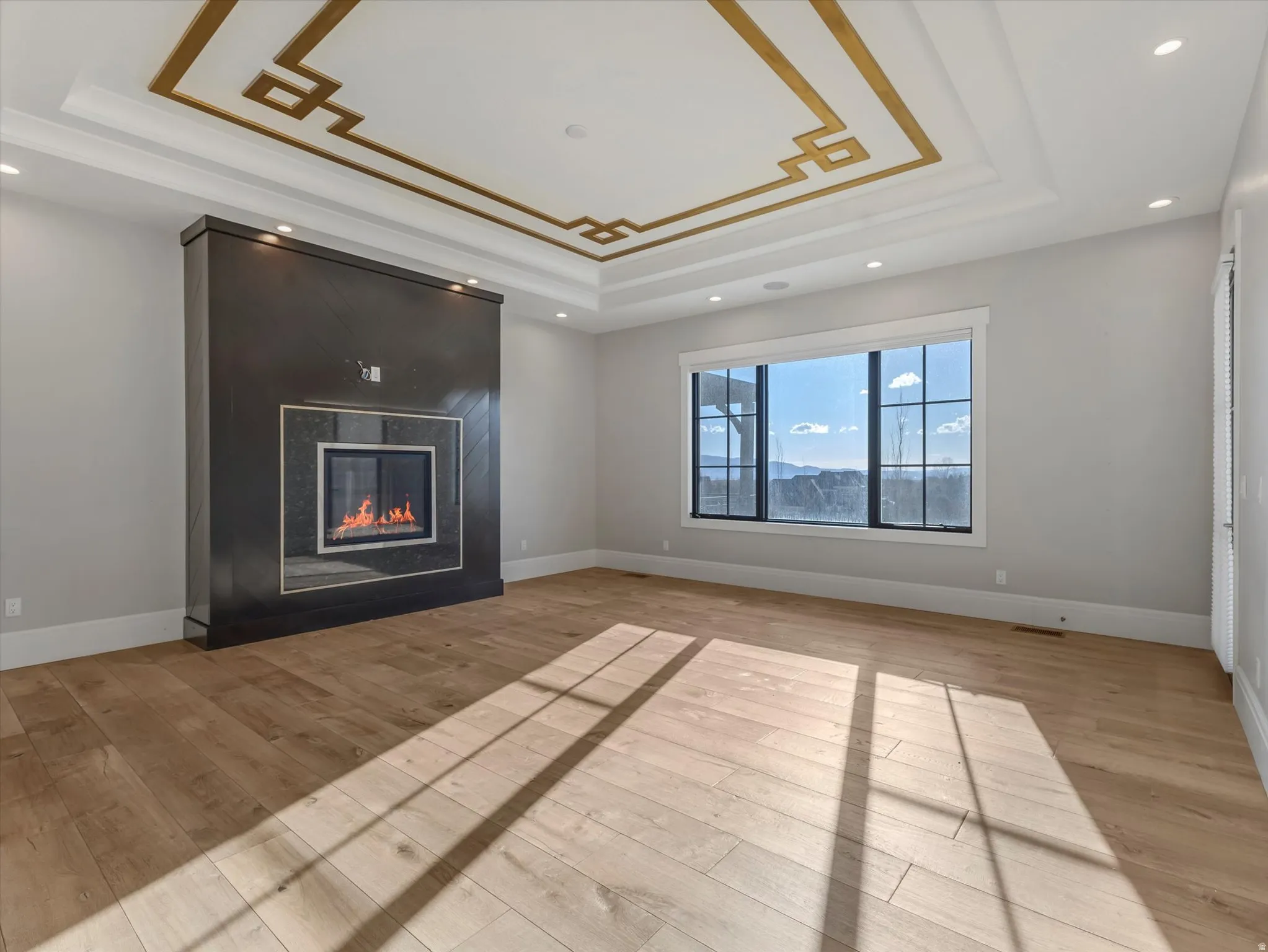 Primary bedroom featuring light wood-style floors, a large fireplace, recessed lighting, and a raised ceiling