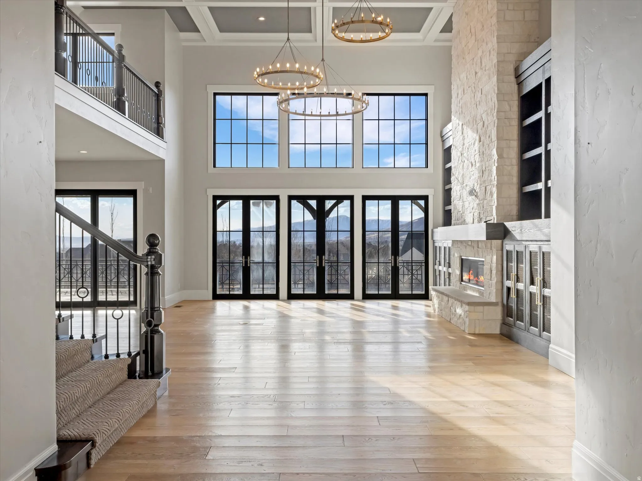 Front door entrance to living room with healthy amount of natural light, hardwood / wood-style floors, a stone fireplace, suspended lighting, and high coffered ceiling